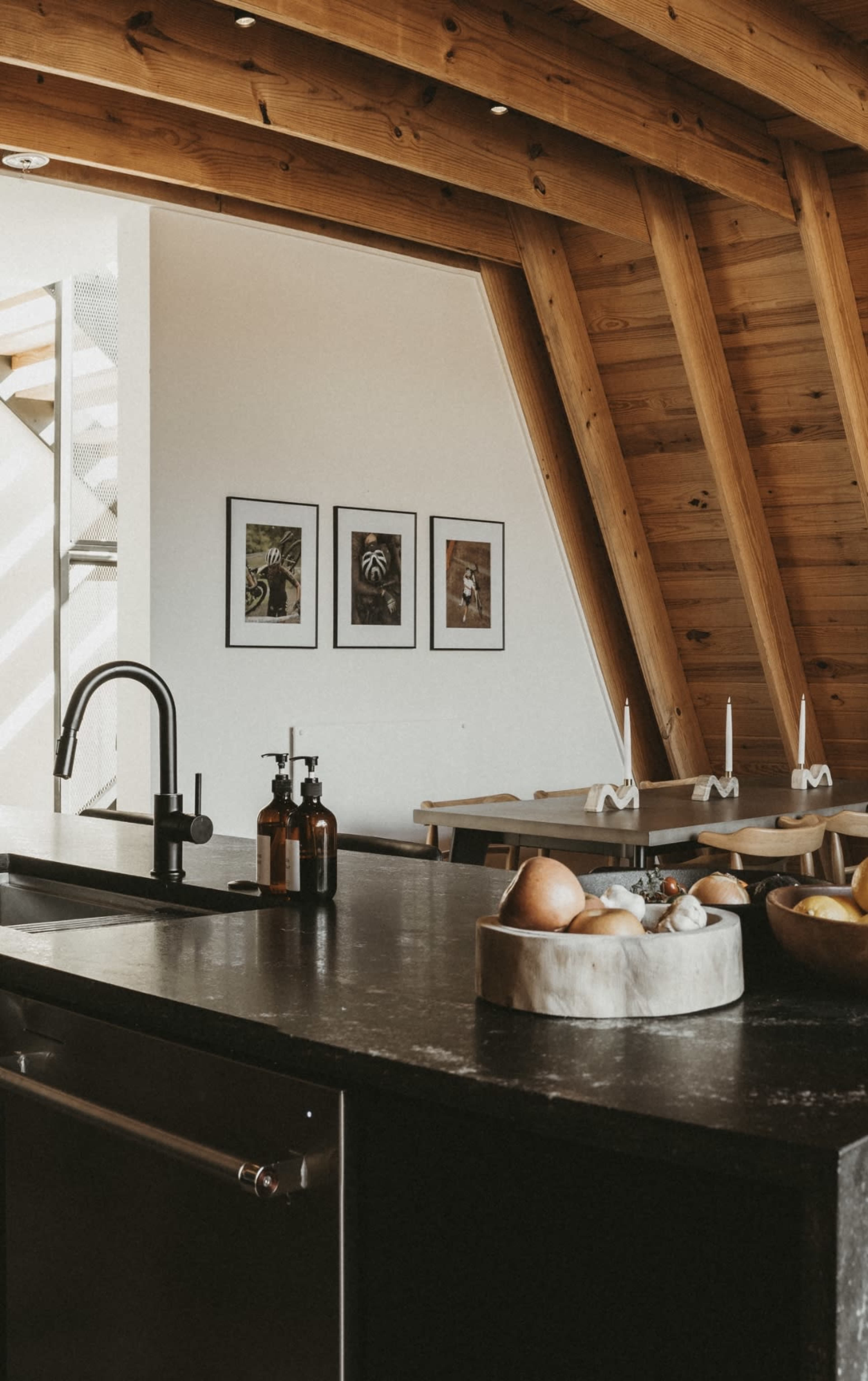 A modern kitchen with a sleek black countertop, wooden beams, and framed photographs on the wall.