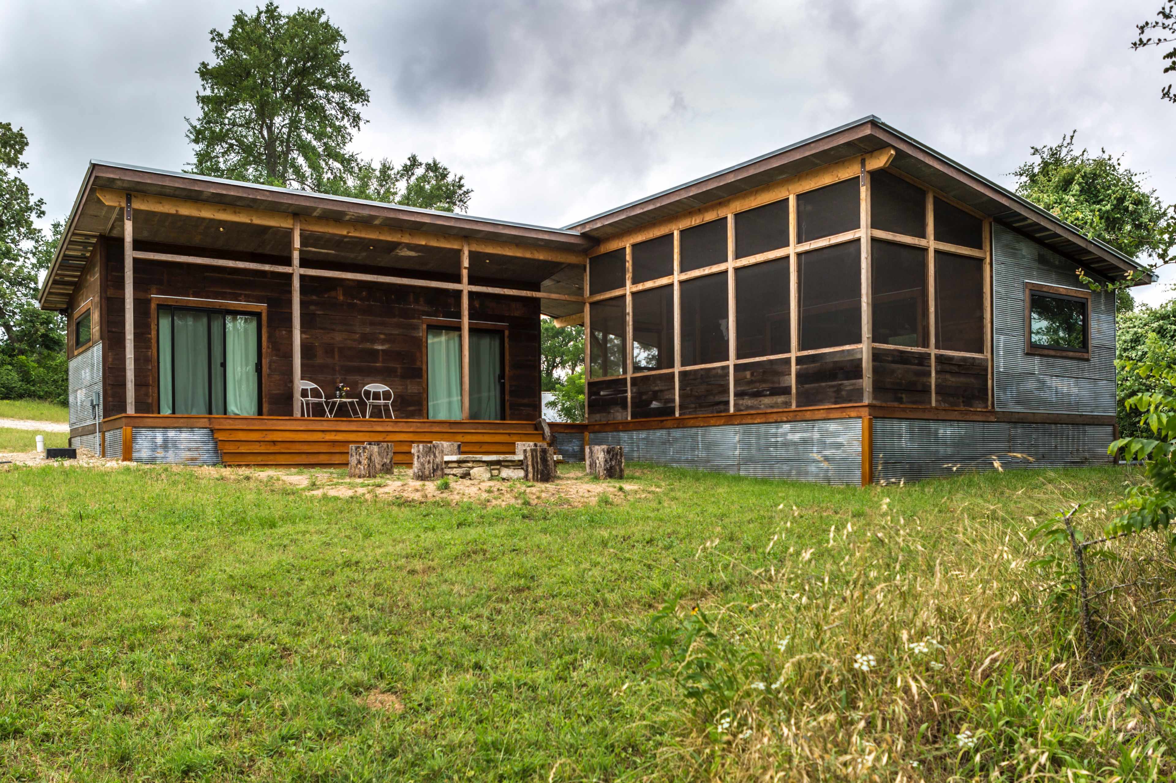 A modern house with a wooden porch, a screened-in area, and large windows set in a green landscape.