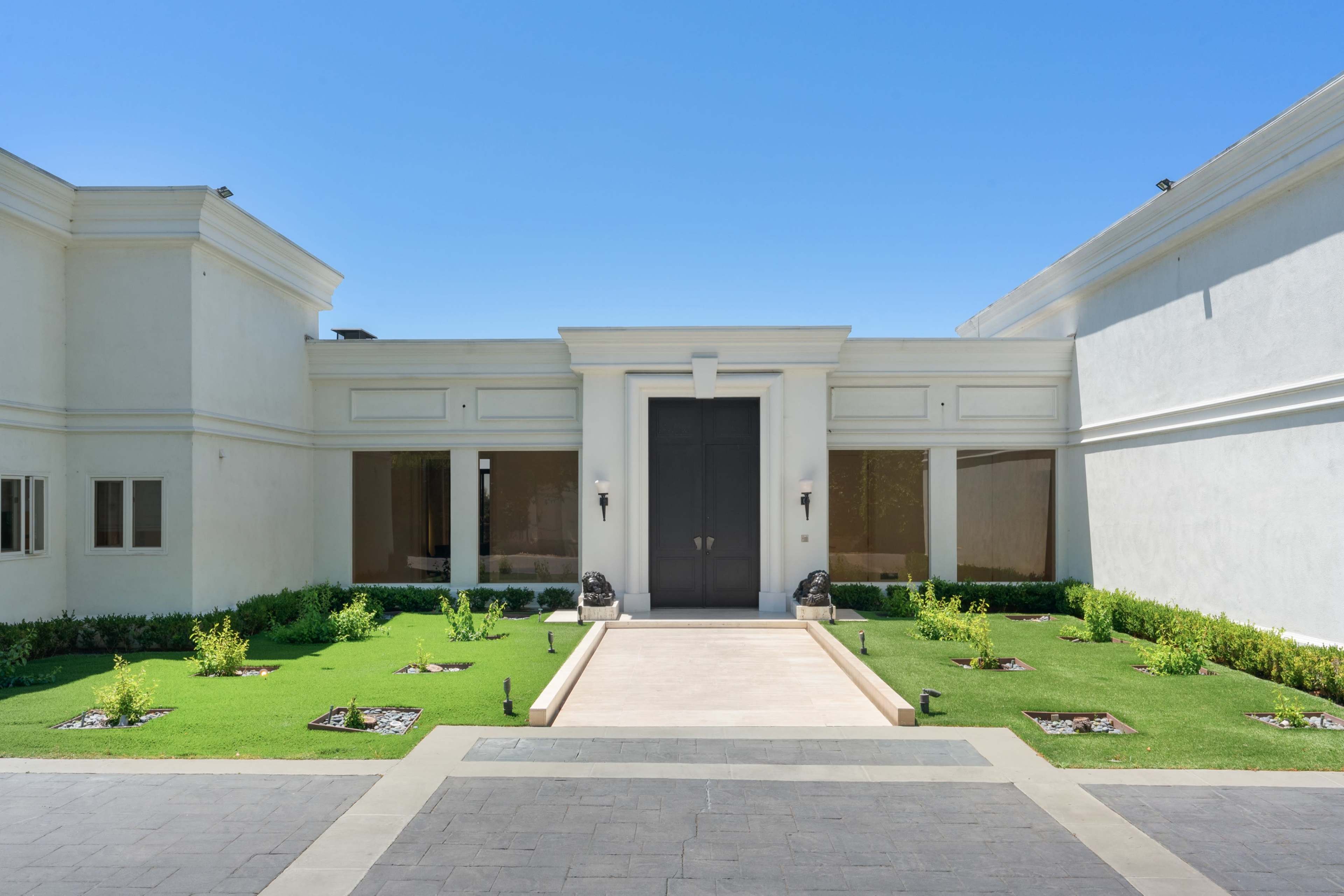 A modern building entrance with a large double door, flanked by greenery and a stone pathway leading to the door.