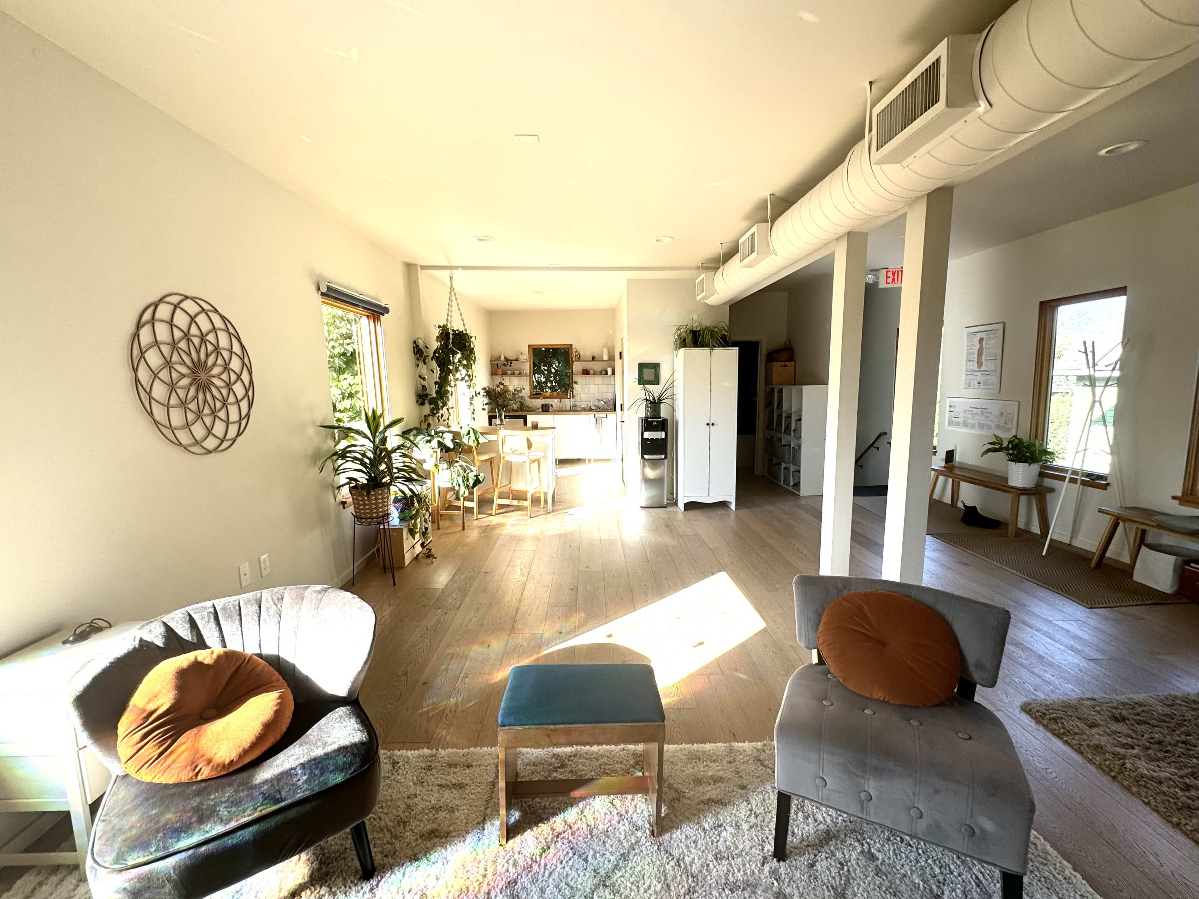 The image shows a bright, minimalistic room with two chairs, a small table, and a kitchen area visible in the background.