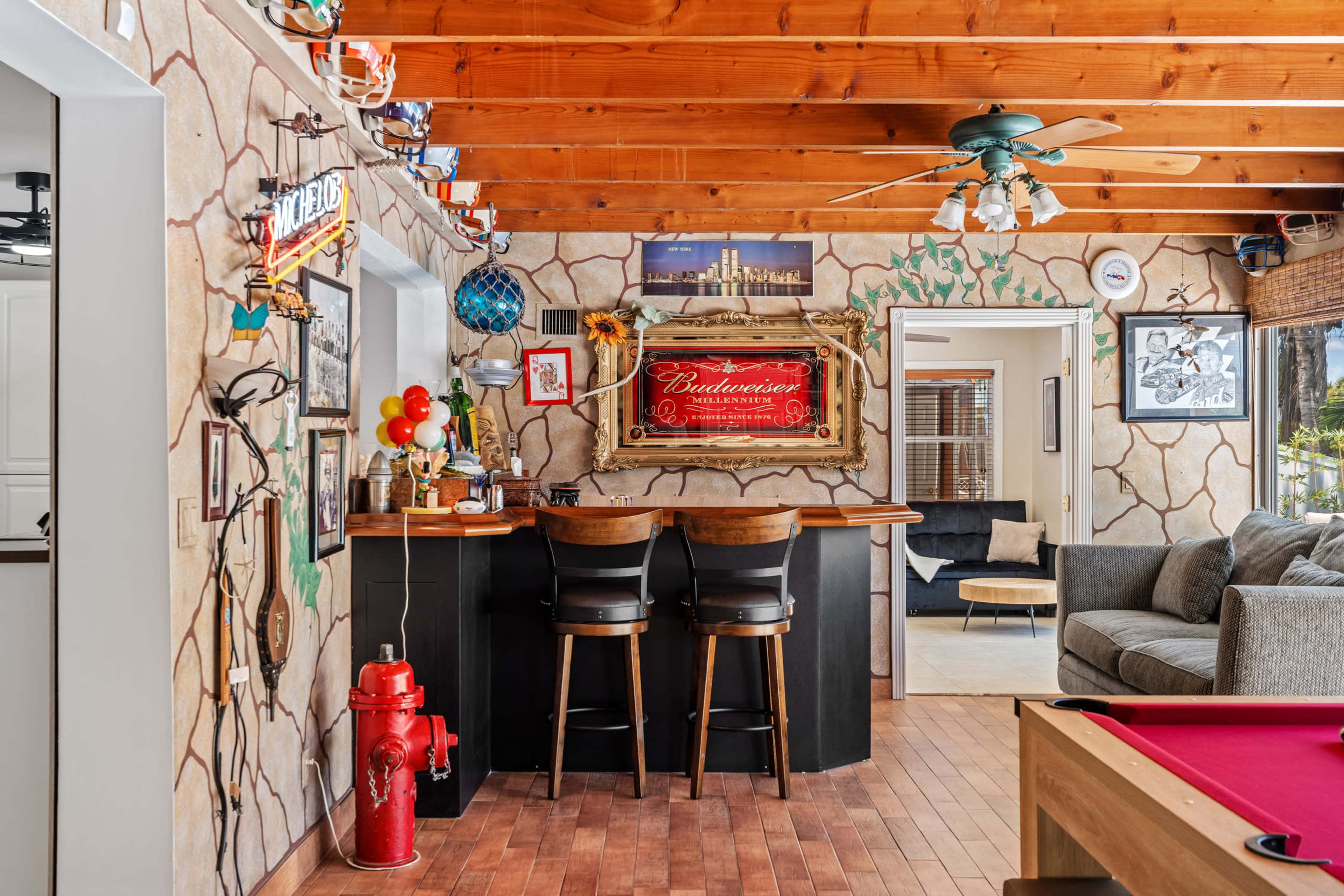 The image shows a rustic-themed bar area with two high stools, decorative wall art, and a pool table in a cozy room with wooden beams and a fire hydrant.
