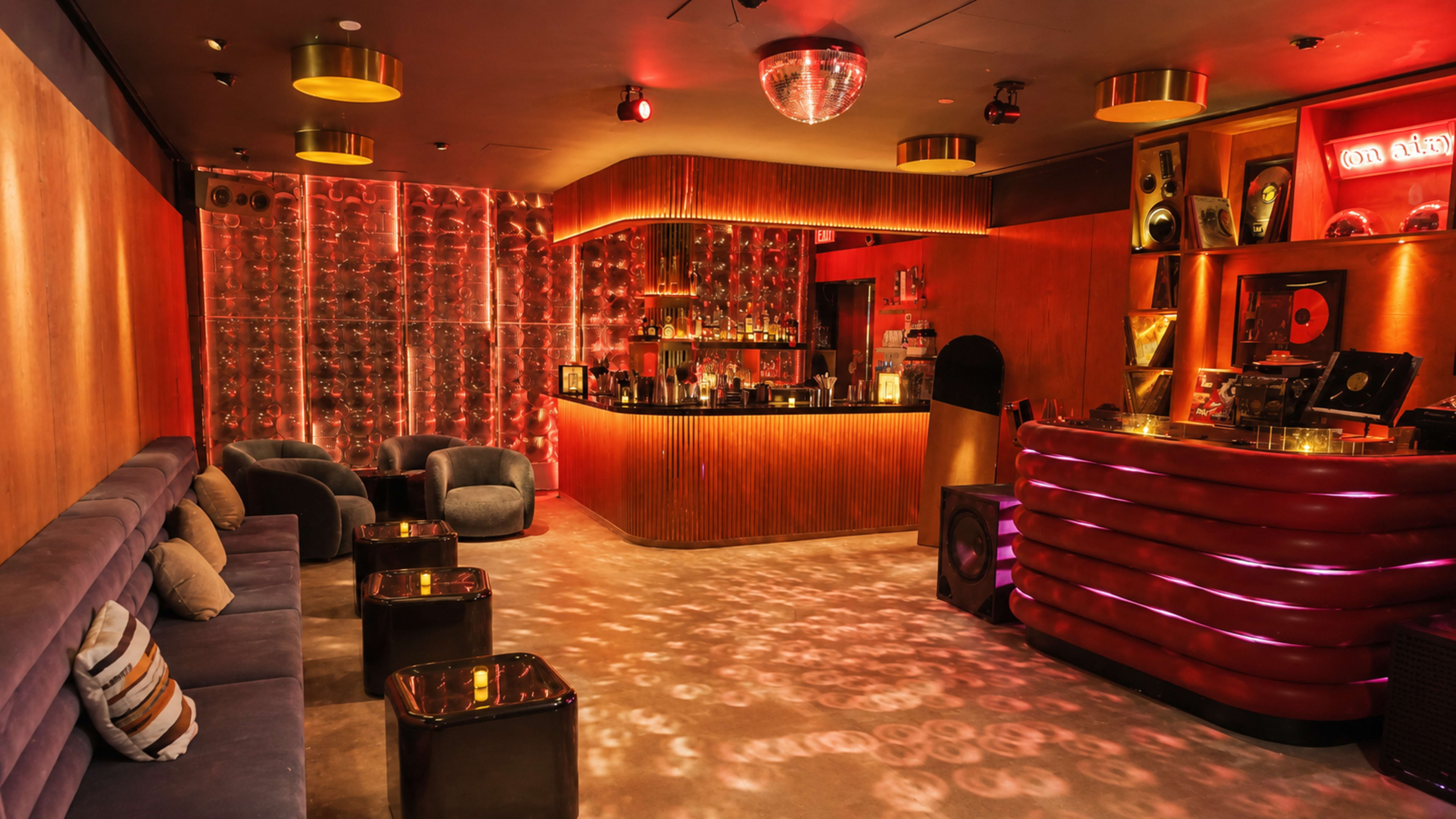 The image shows a stylish bar area with a circular counter, plush seating, and decorative lighting, creating a vibrant nightlife atmosphere.