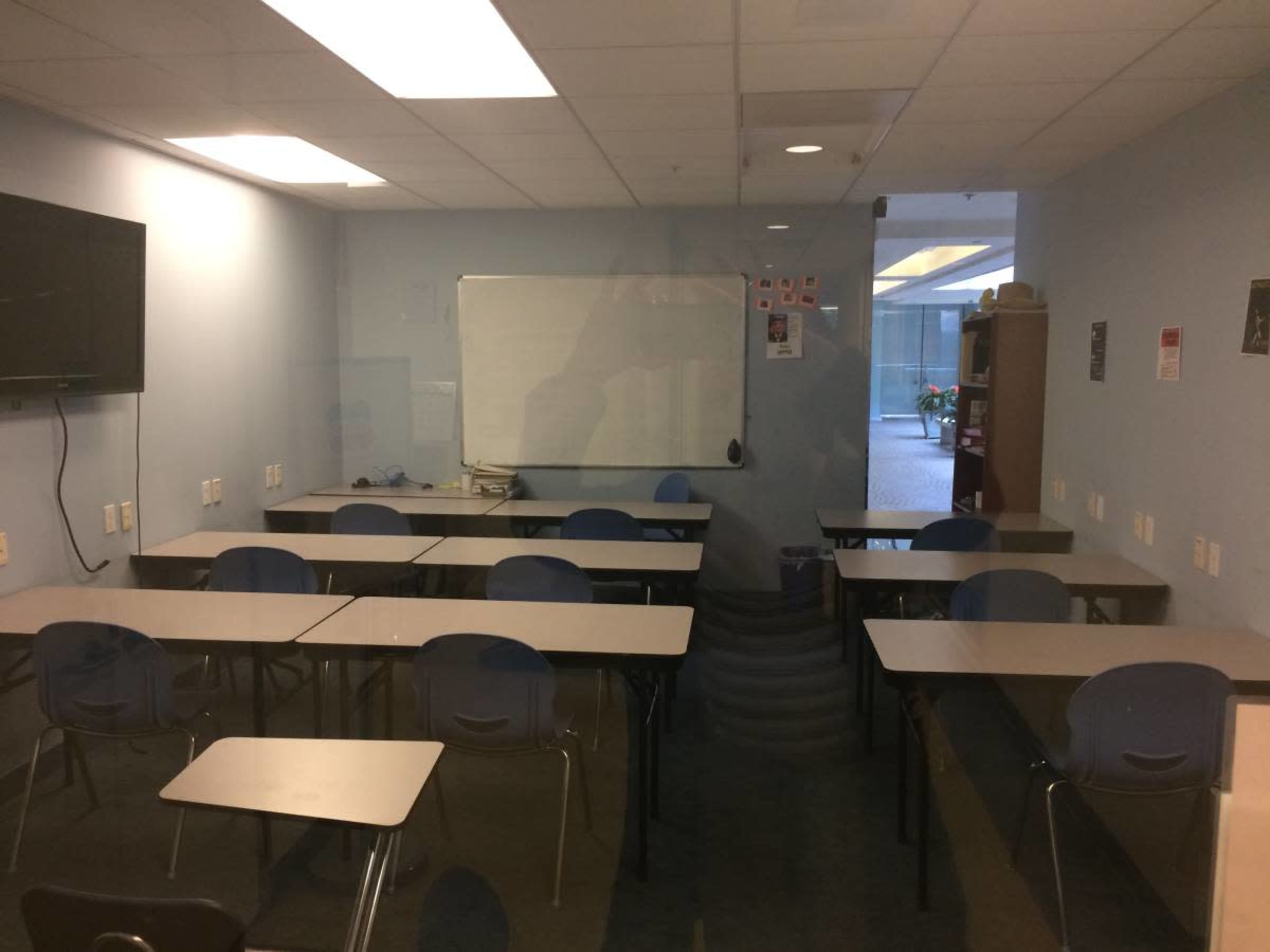 The image shows a classroom with empty desks arranged in rows and a whiteboard at the front.