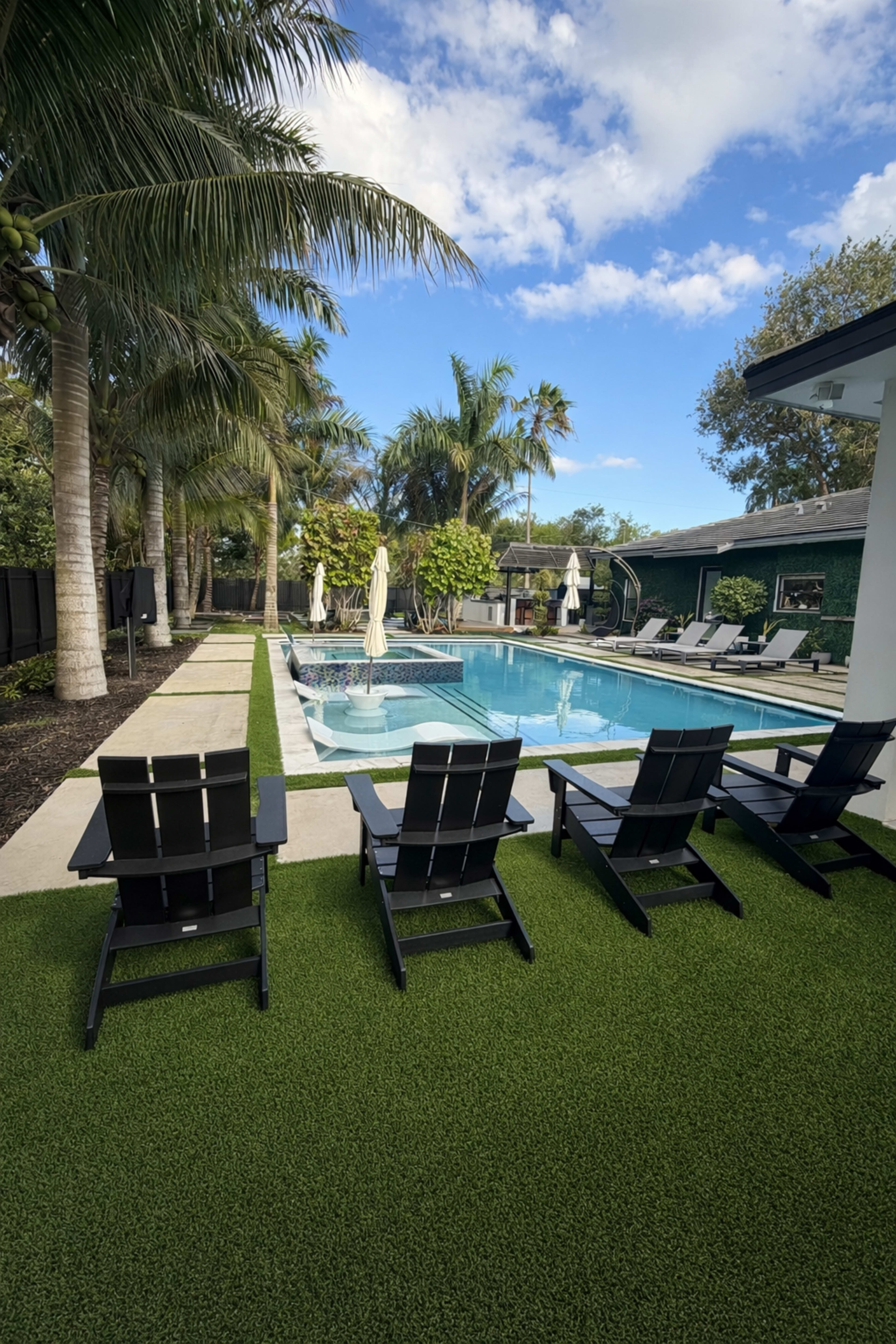 The image shows a backyard with a swimming pool bordered by palm trees, lounge chairs, and manicured grass.