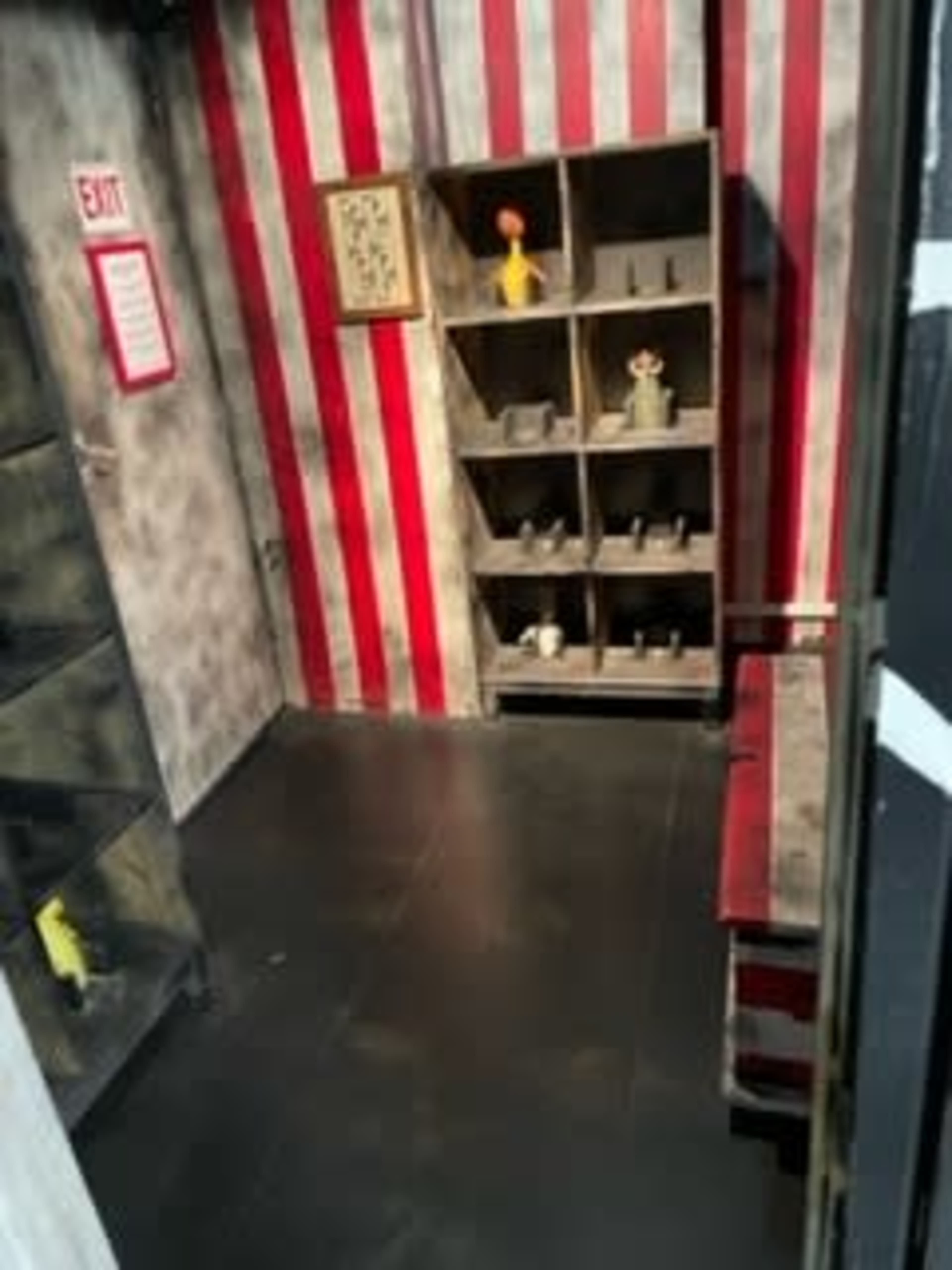 A room with red and white striped walls, featuring a shelf with various objects and a sign indicating the exit.