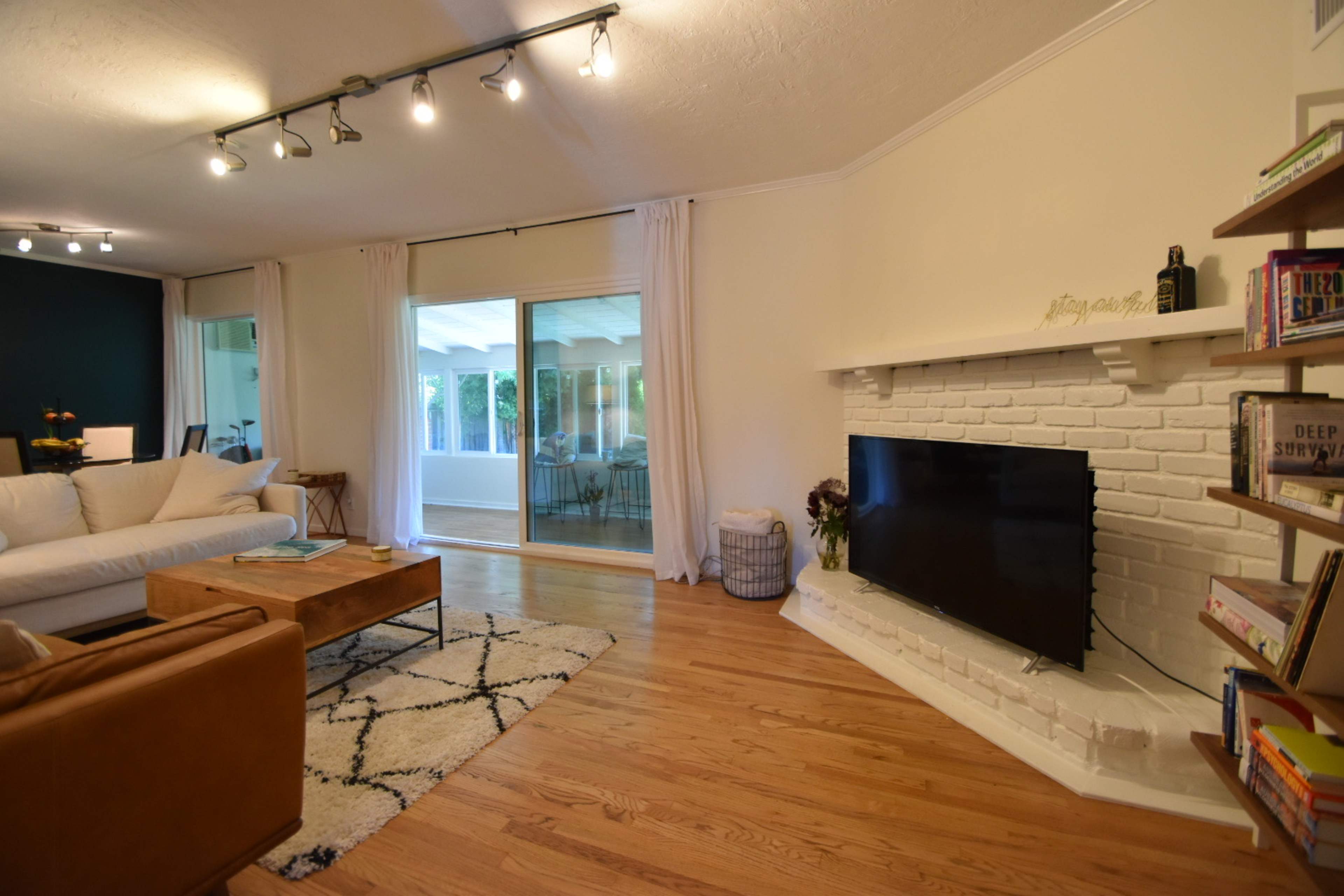 The living room features a white brick fireplace, a television mounted above it, and a seating area with a coffee table and patterned rug.