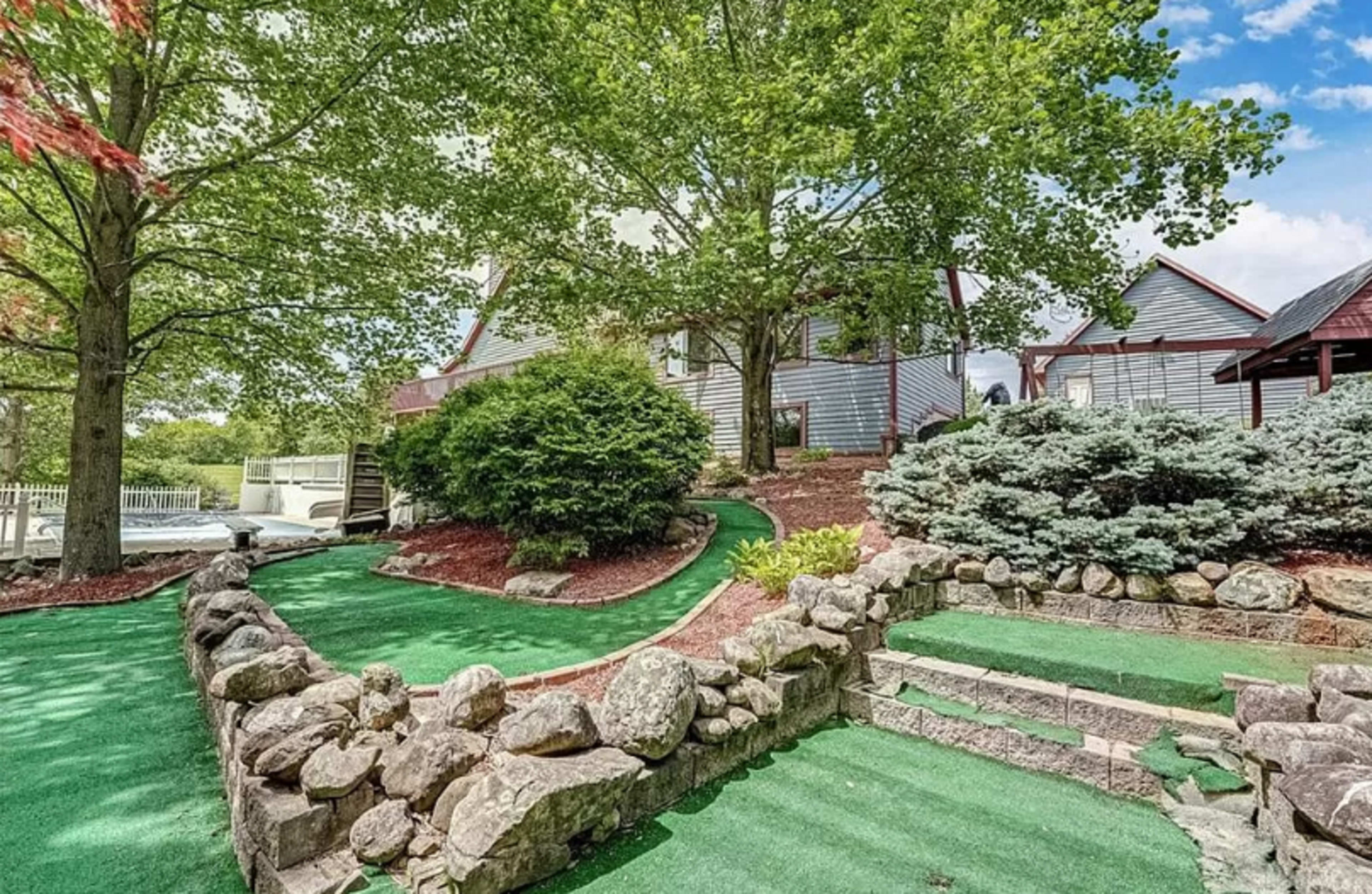 A landscaped backyard featuring a mini-golf area with artificial turf, stone pathways, and lush greenery.