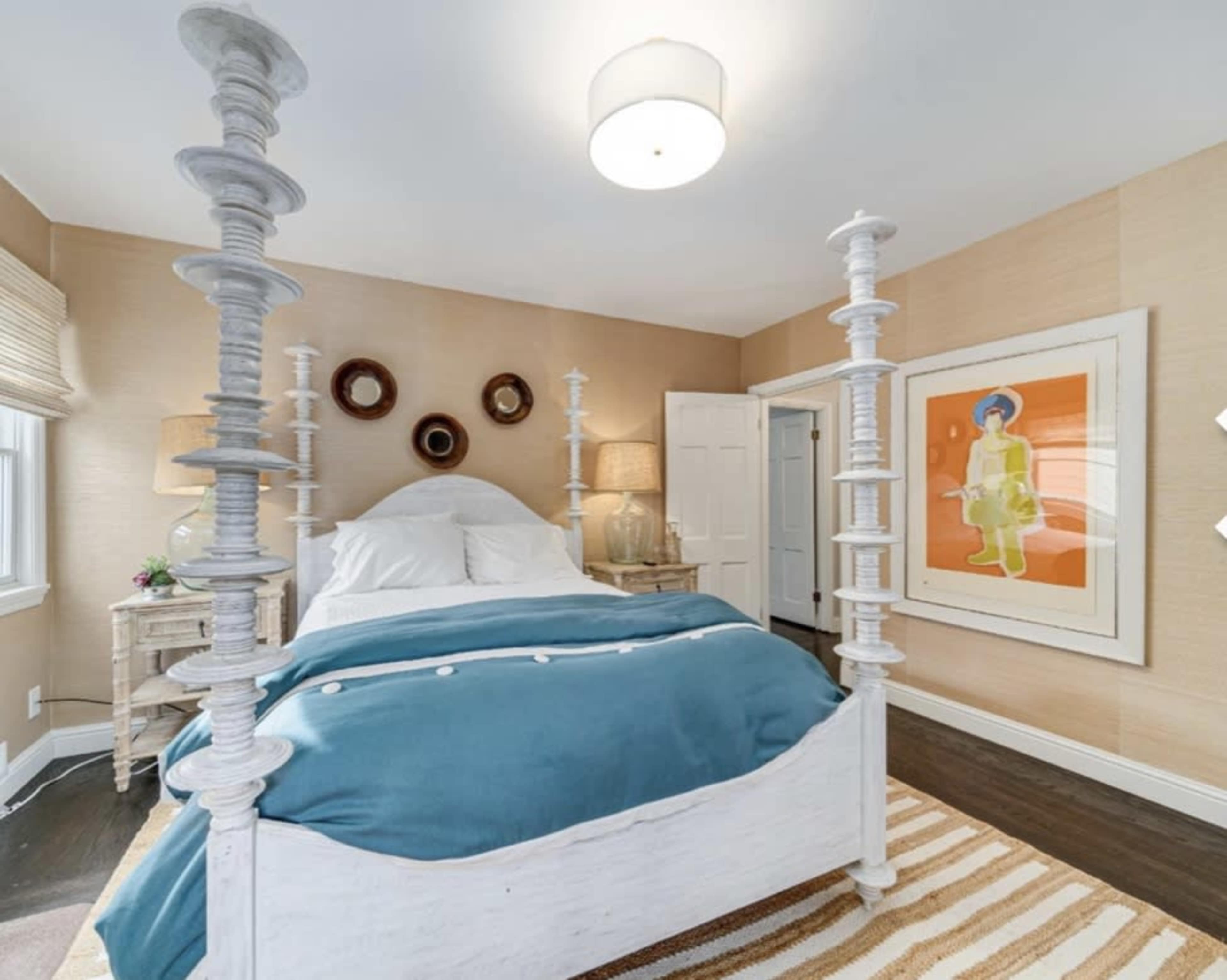 A well-decorated bedroom featuring a four-poster bed with white wooden posts, a blue and white bedspread, and artwork displayed on the walls.