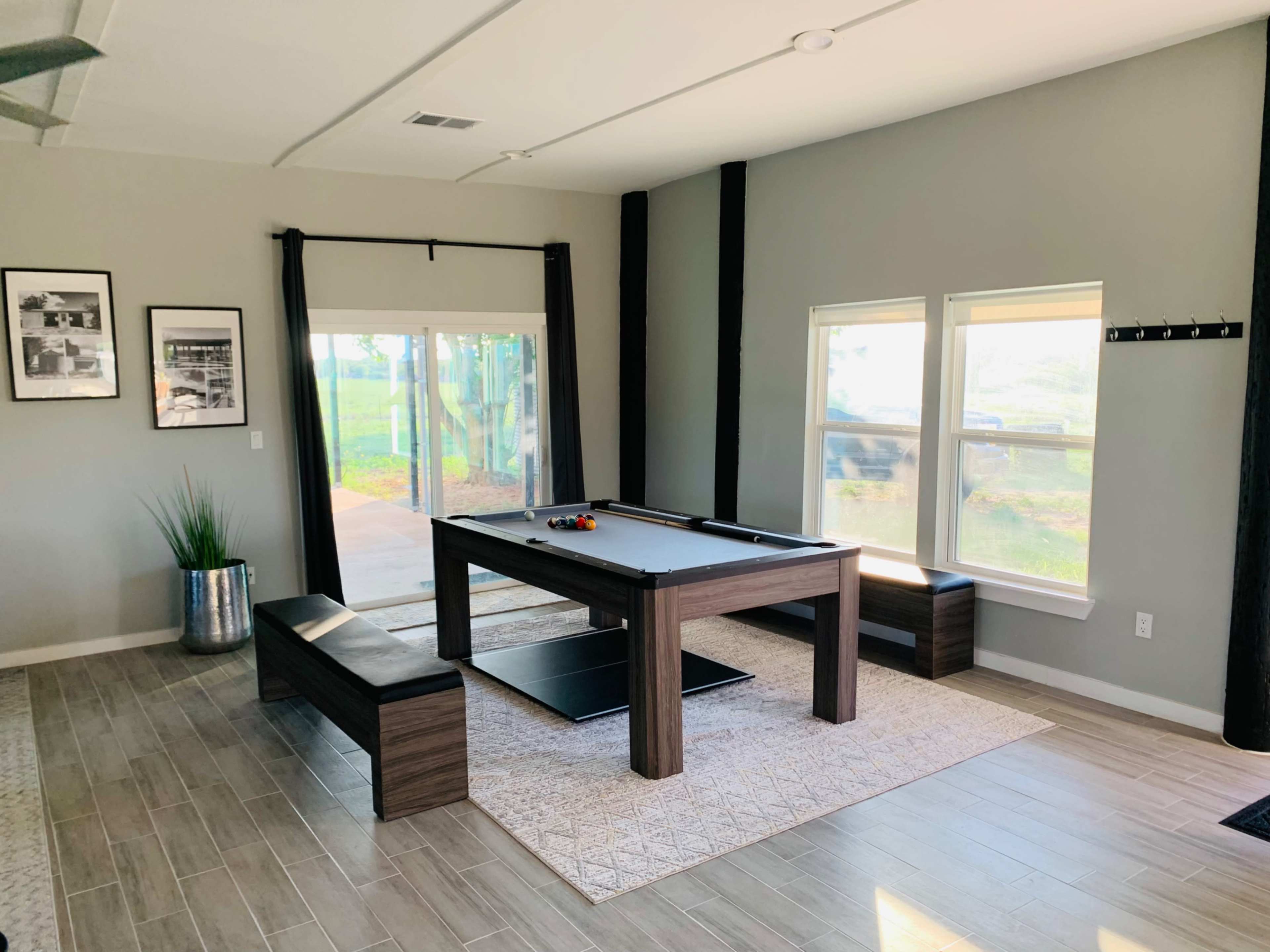 The image shows a modern game room featuring a pool table, benches, and large windows with natural light.