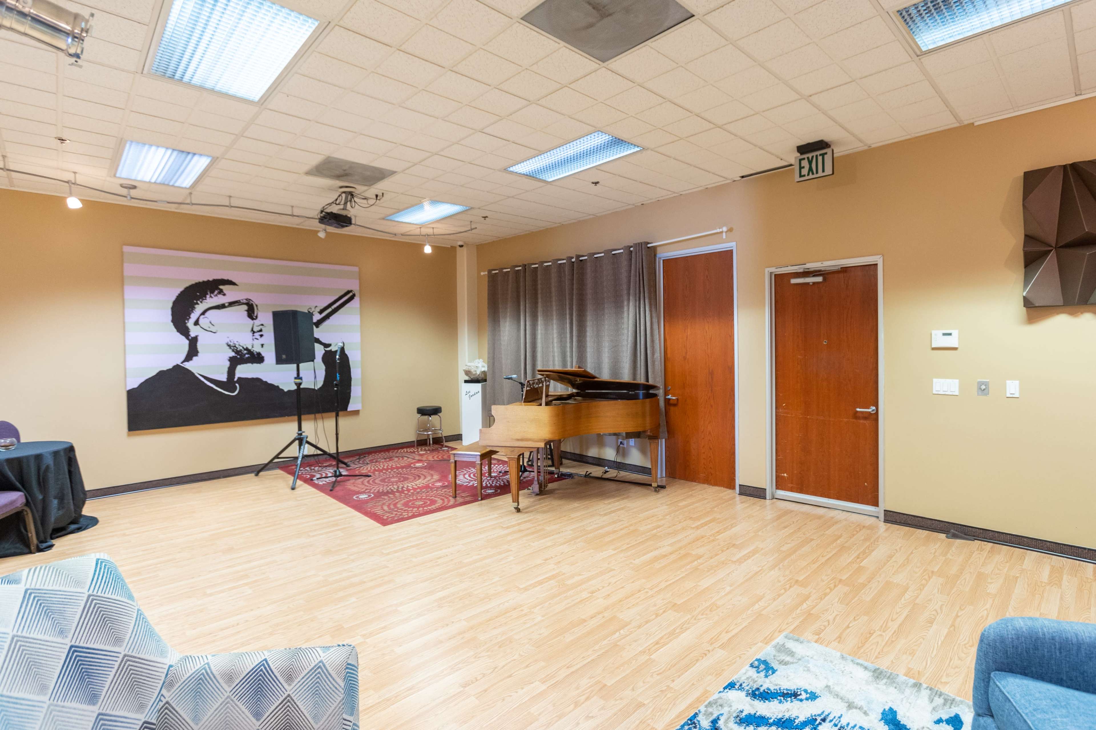 A music rehearsal room featuring a grand piano, a microphone on a stand, and a large wall mural of a person playing a saxophone.