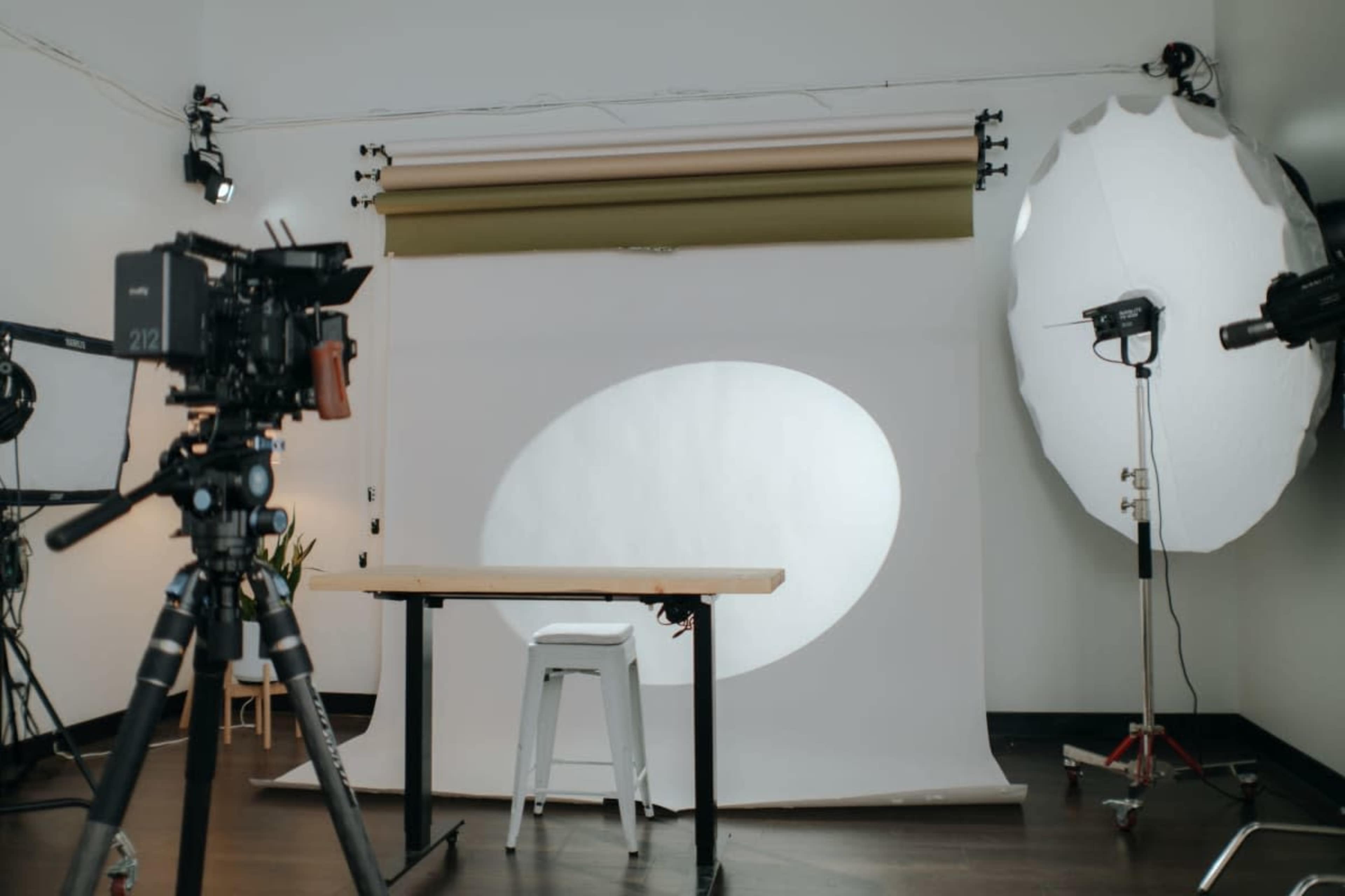 A photography studio is set up with a white backdrop, a table, a chair, and various lighting equipment.