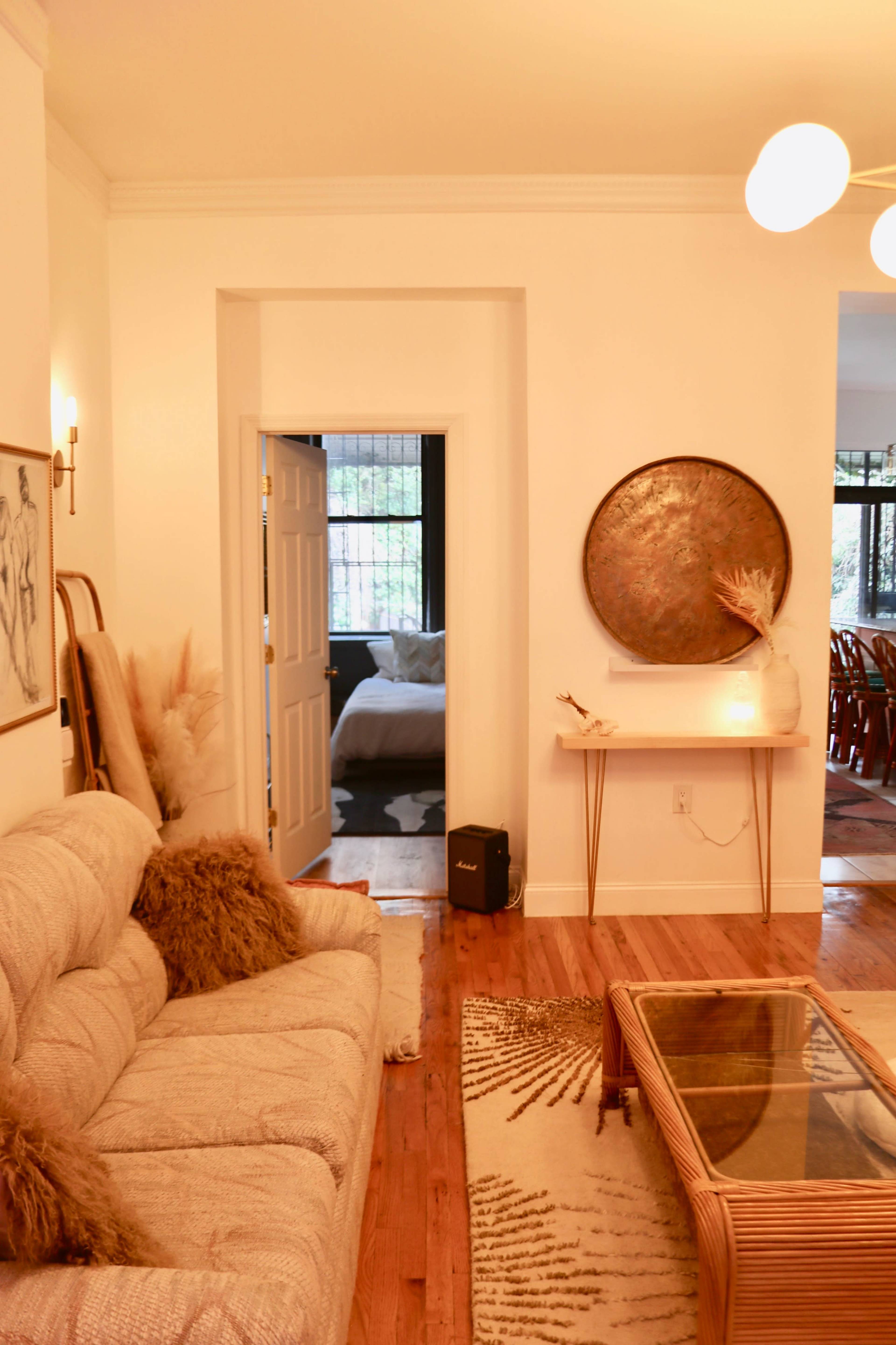 A cozy living room features a beige sofa, a round wall decor, and an open doorway leading to a bedroom in the background.