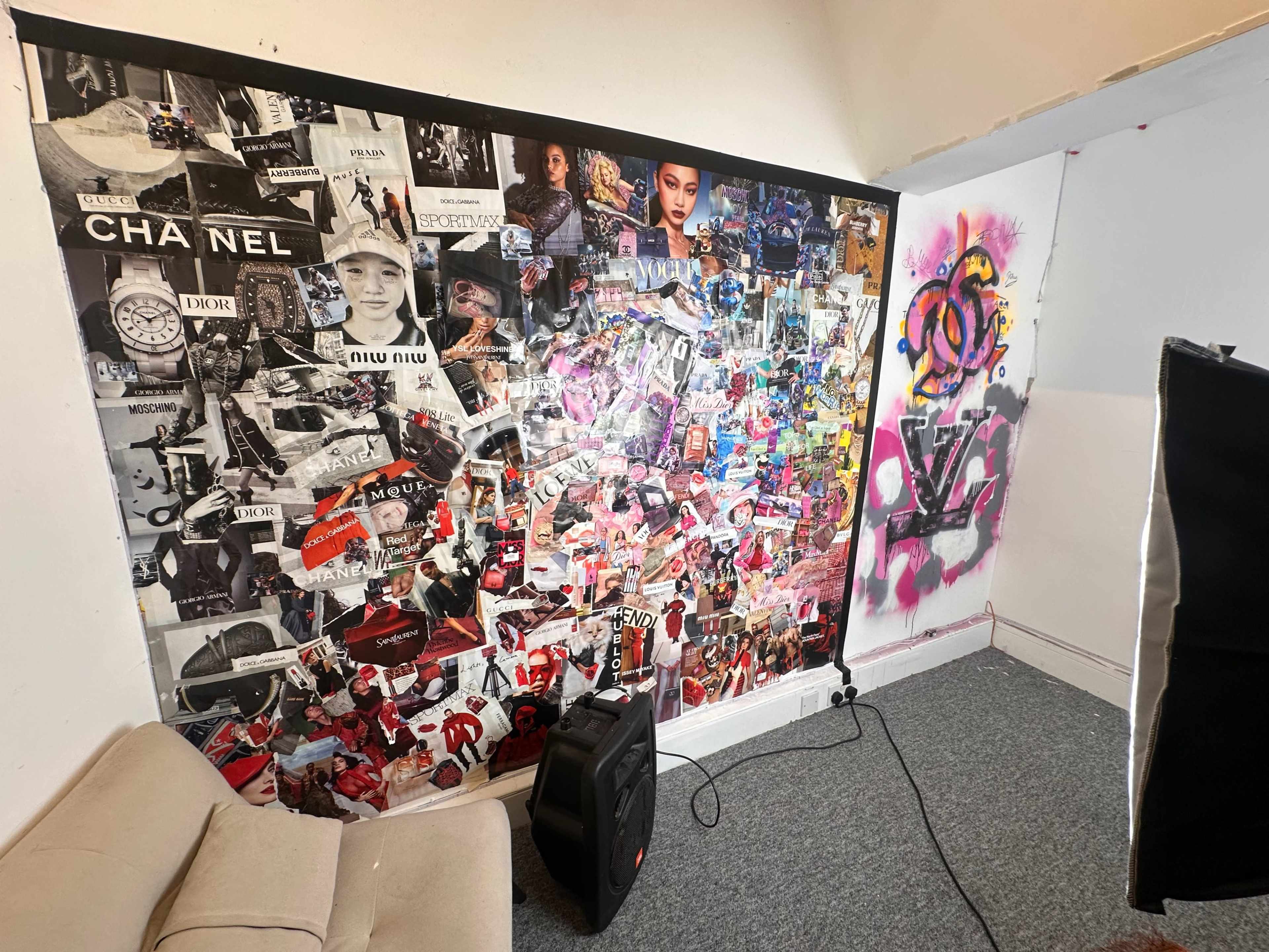 The image shows a collage-filled wall featuring various advertisements, brands, and photographs, with a beige sofa and a speaker placed in front of it.