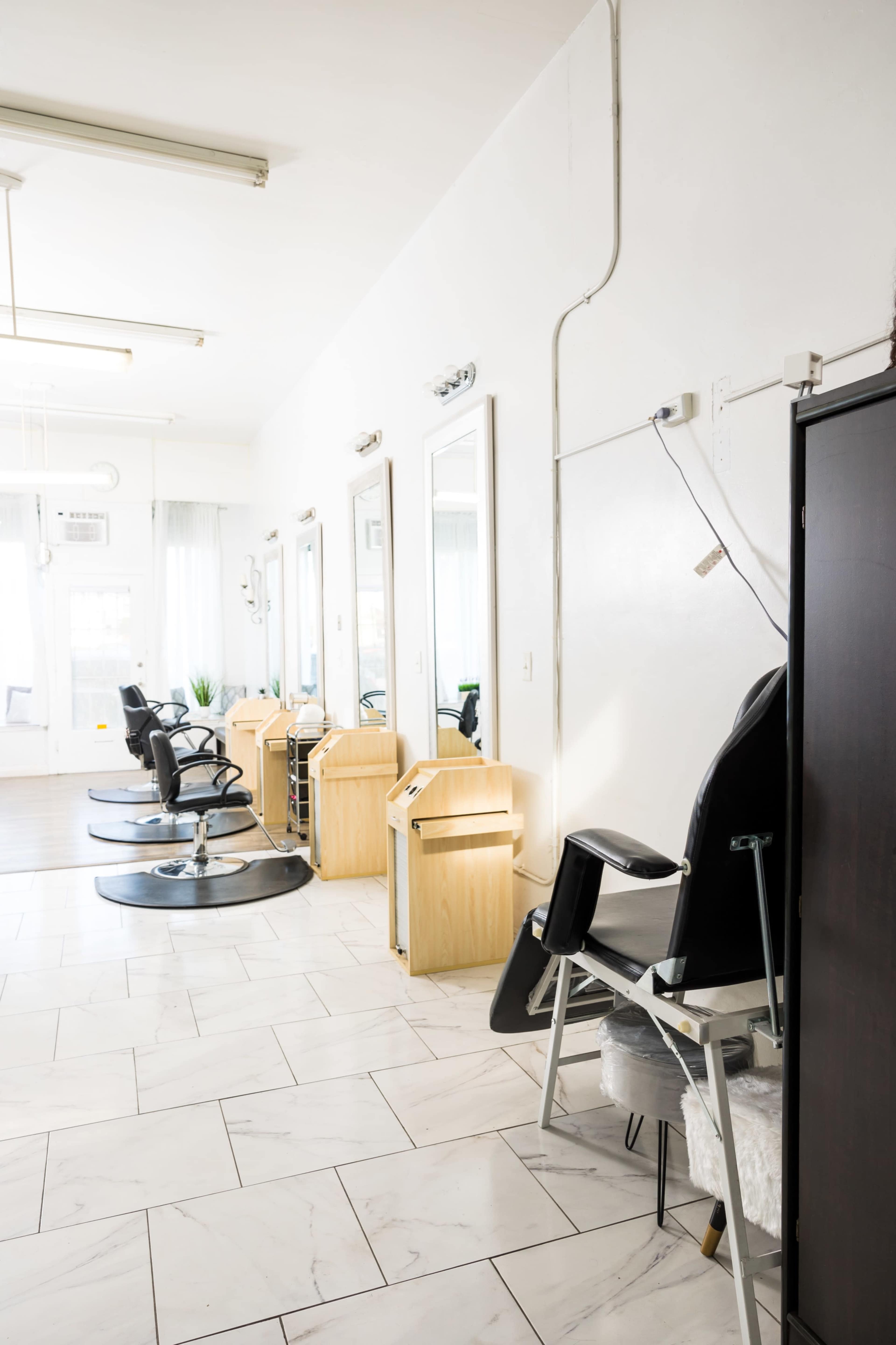 The image shows a brightly lit hair salon with four styling stations featuring mirrors and black salon chairs along one wall.