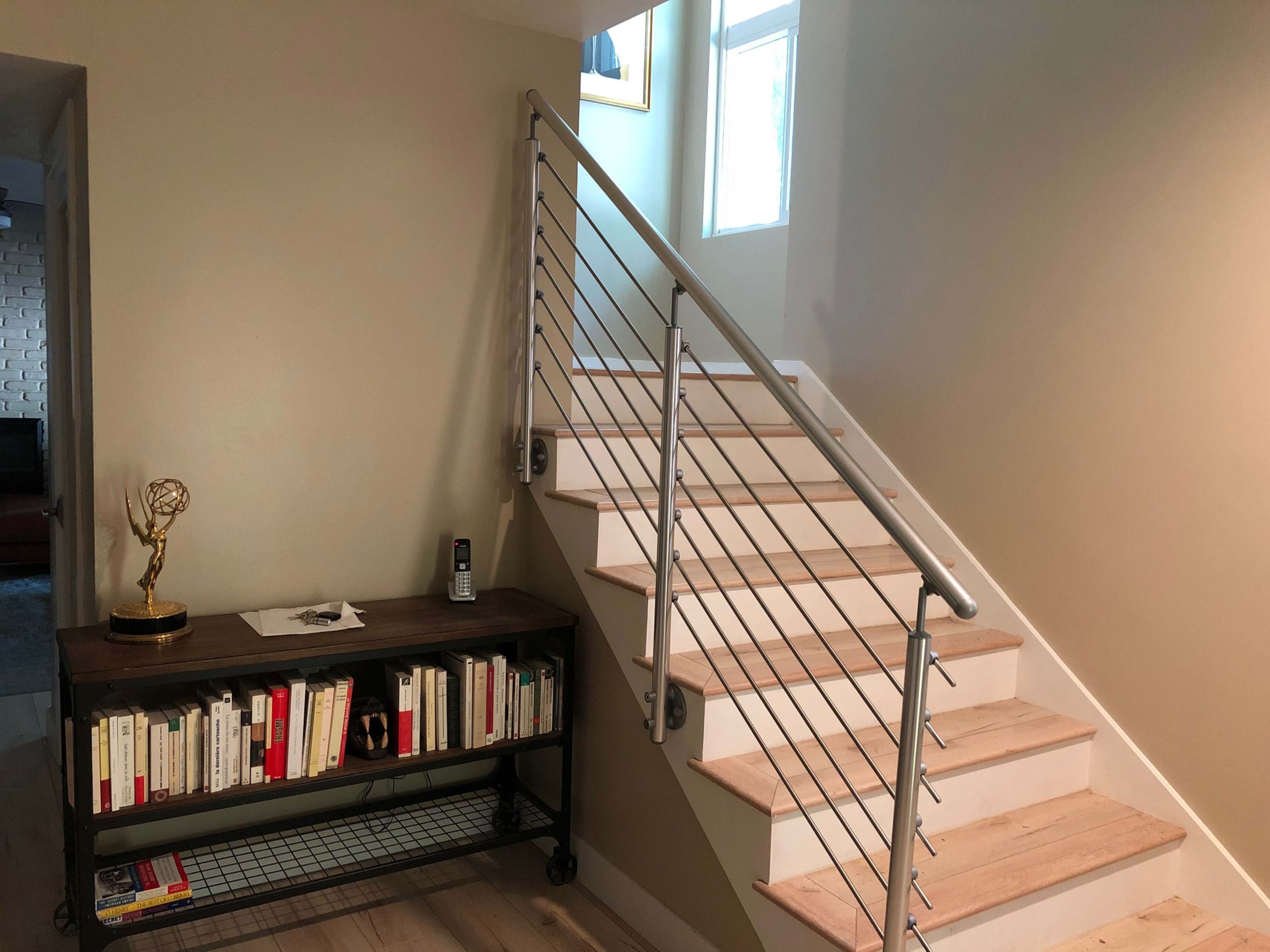 A staircase with a metal railing next to a wooden table holding books and a decorative item, against a wall painted in a light color.