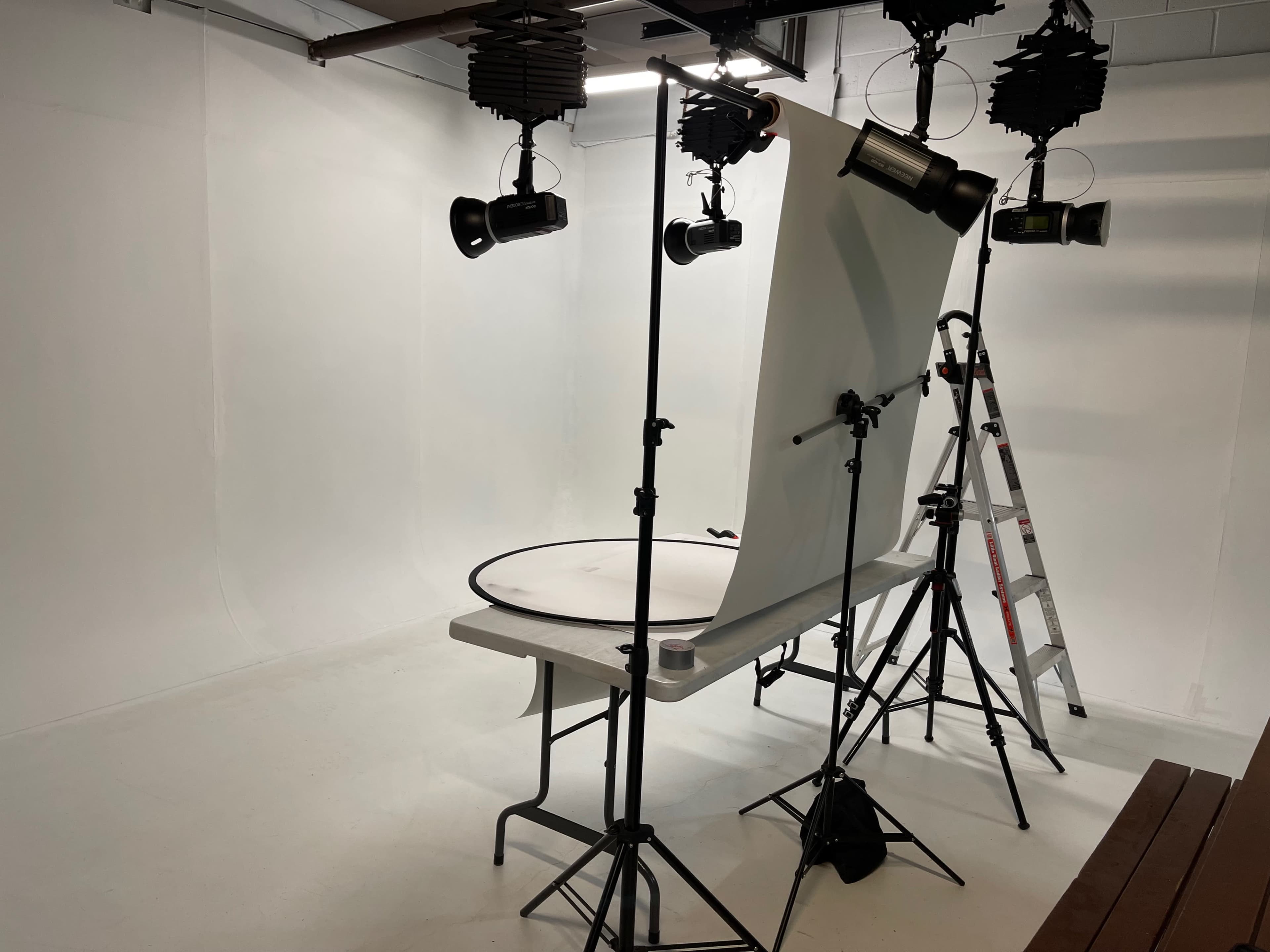 A photography studio setup with a white backdrop, a circular table, and various lighting equipment.