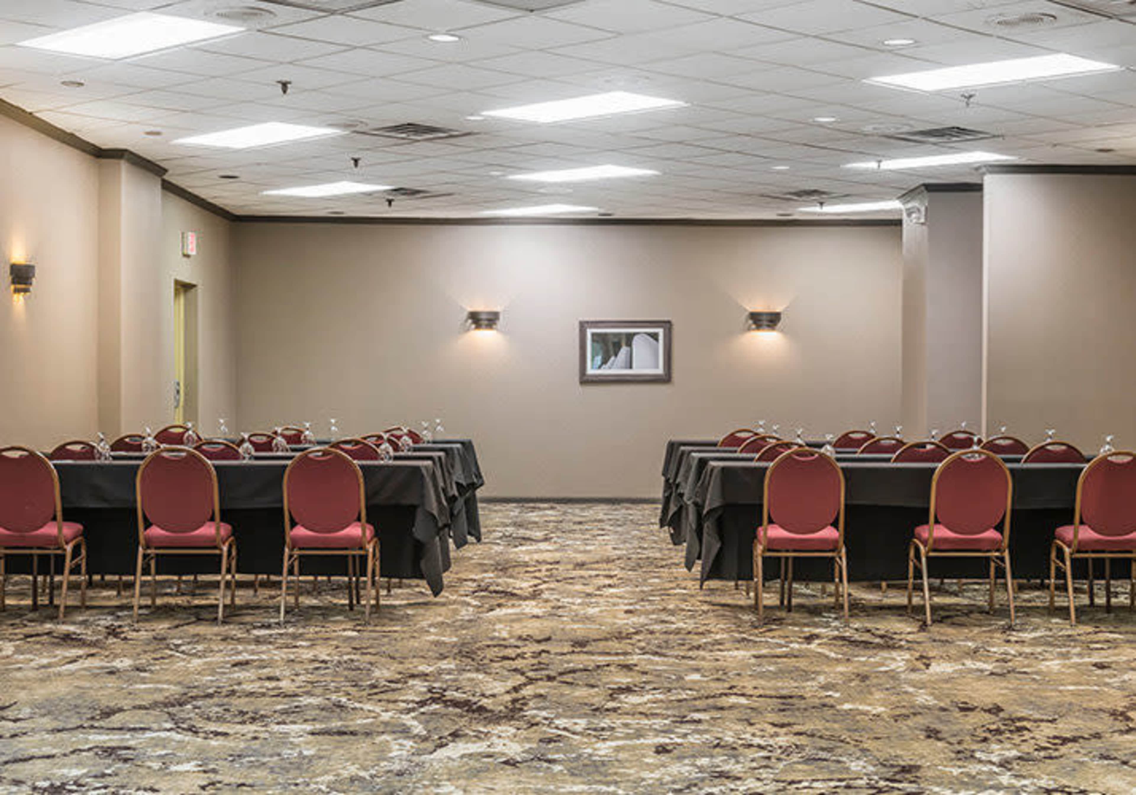 The image shows a conference room set up with rows of tables and chairs, featuring dark tablecloths and red upholstered chairs on a patterned carpet.
