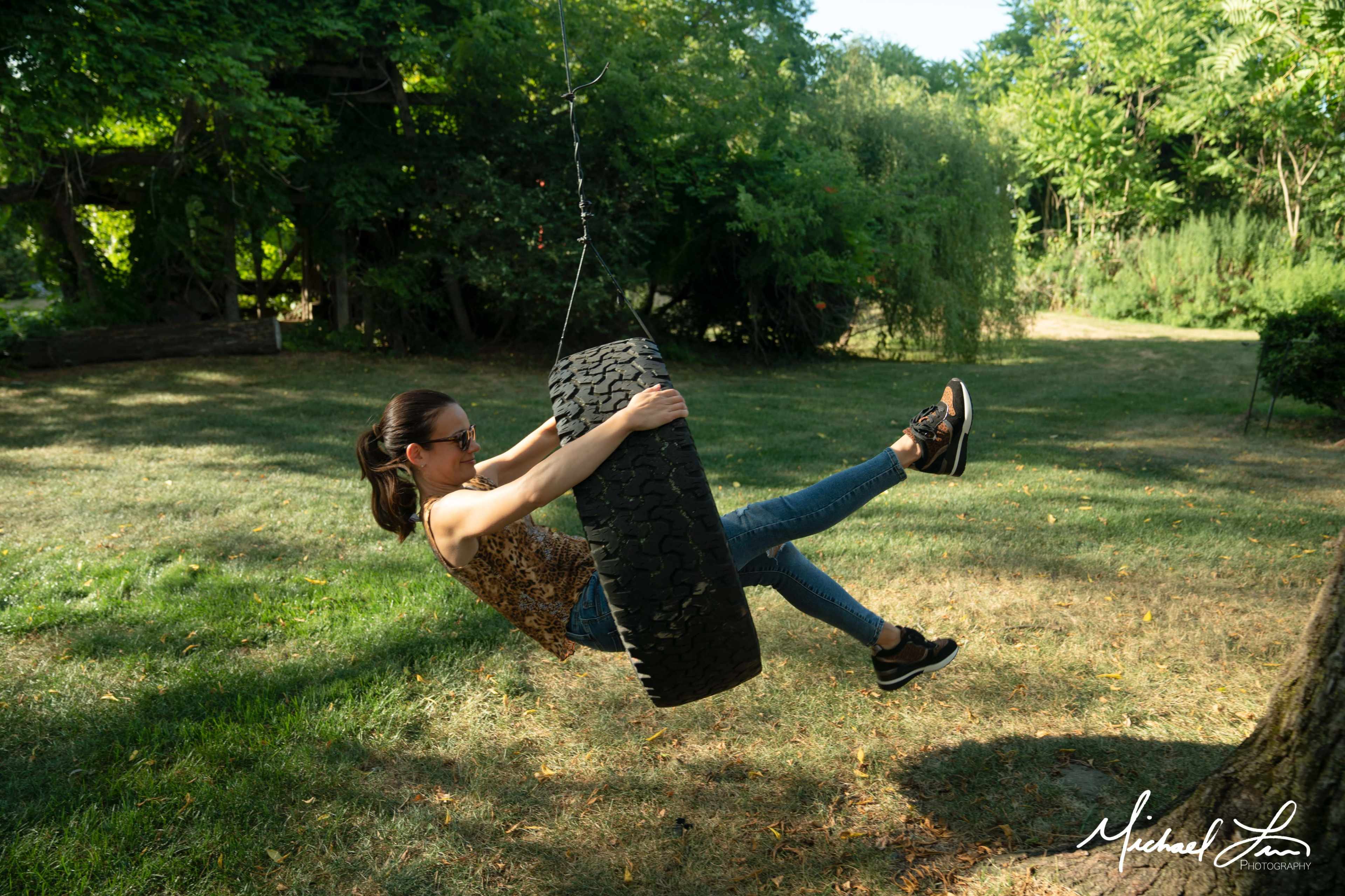 A woman swings on a tire swing hanging from a tree in a grassy area.