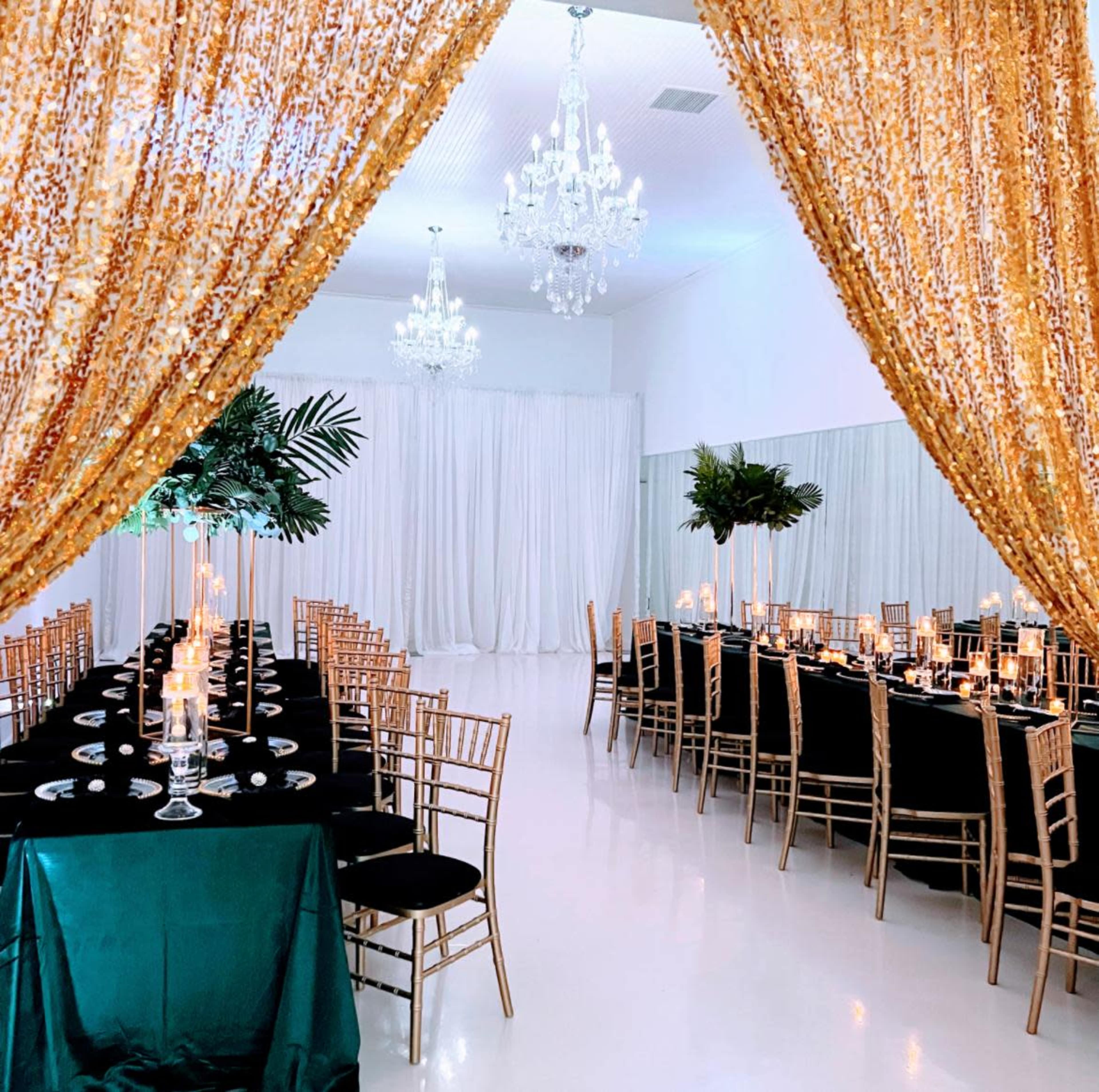The image shows a banquet hall elegantly arranged with long, dark tables, golden chandeliers, and a backdrop of shimmering curtains.