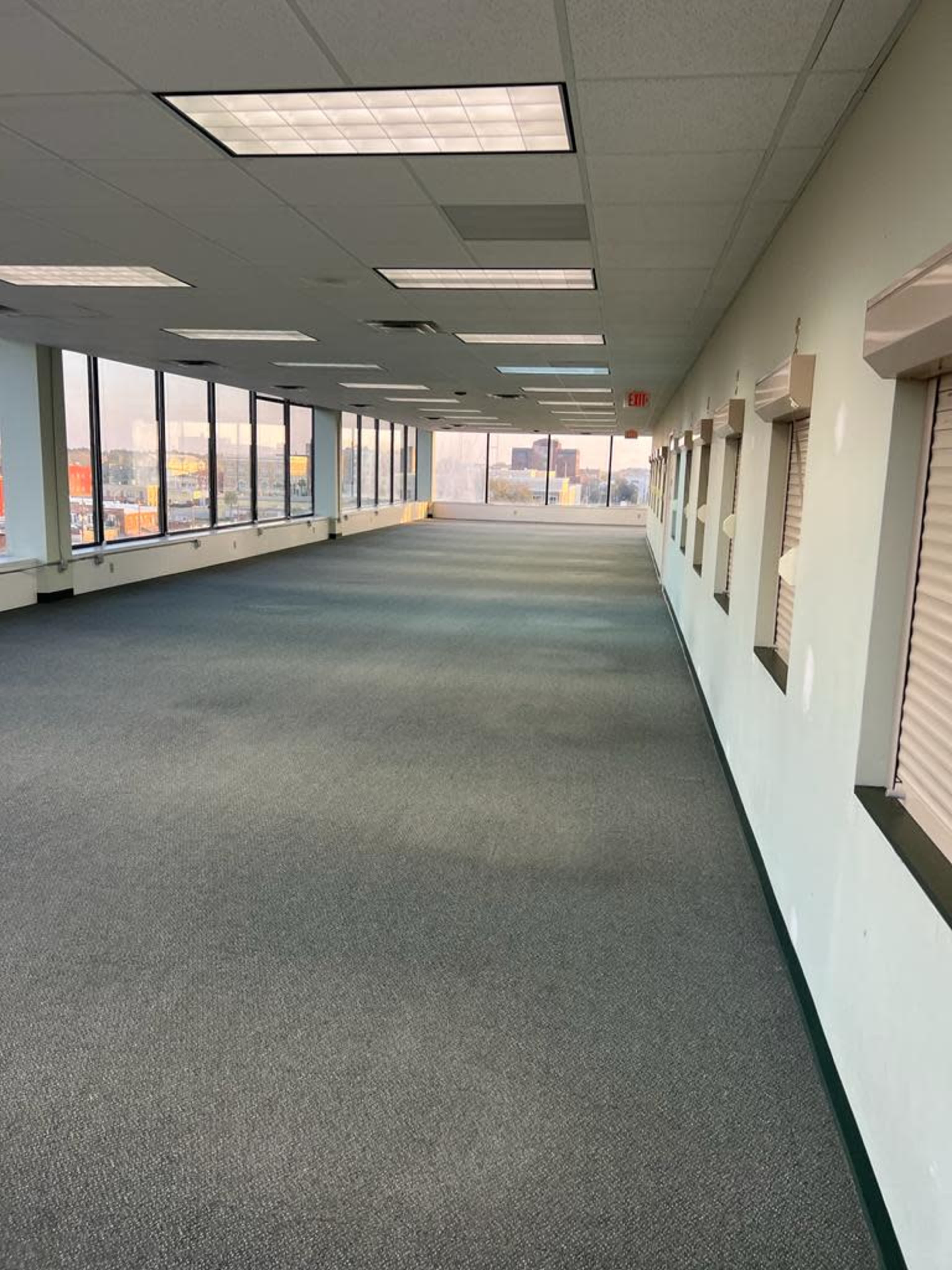 A long, empty corridor with windows on one side and carpeting on the floor.