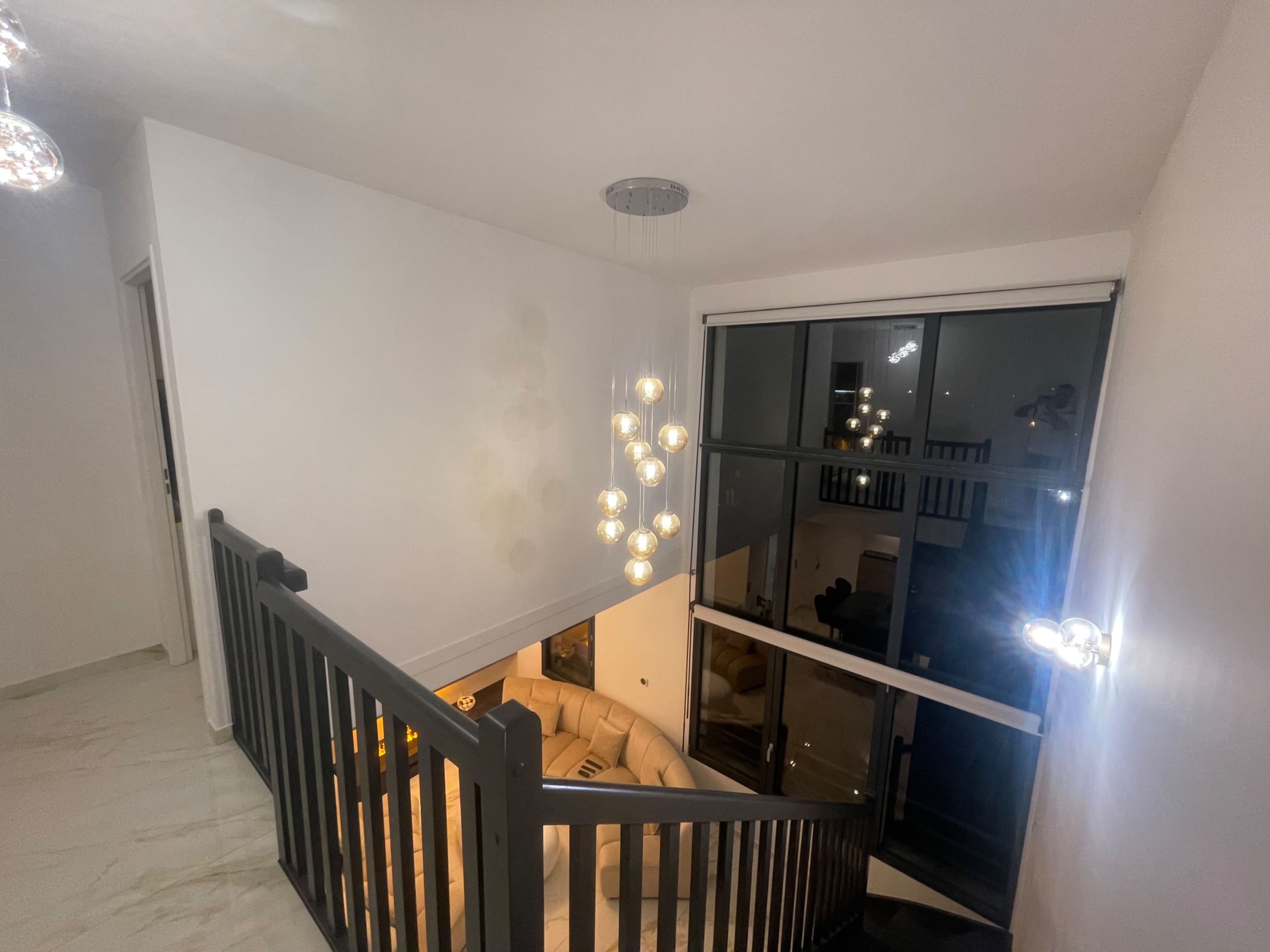 A staircase leads down to a living area illuminated by pendant lights, with large windows providing a view of the interior space.