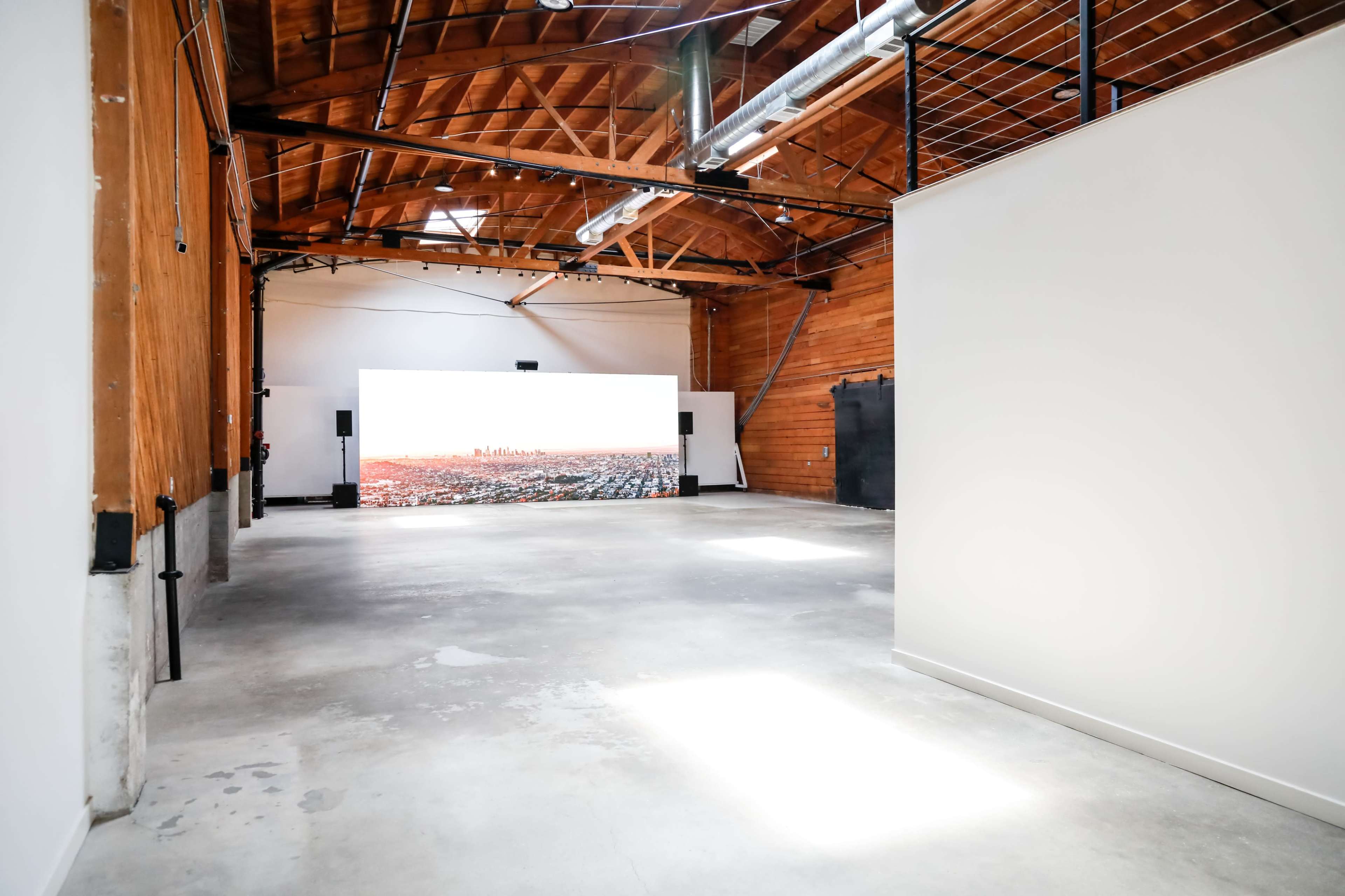 A spacious interior of an art gallery with wooden beams and a large backdrop installation at one end.