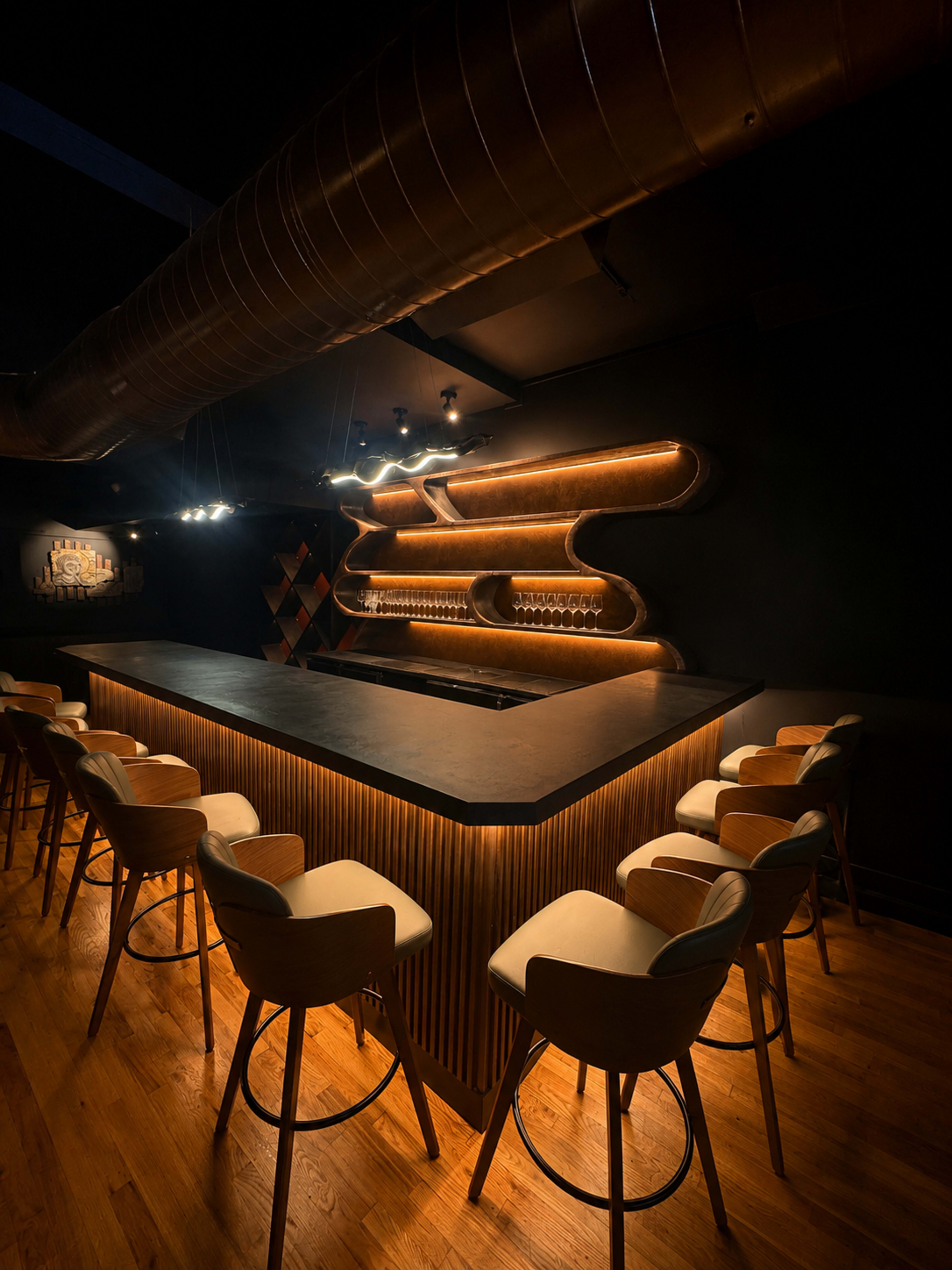 The image shows a modern bar with a sleek, illuminated counter and seating arranged around it, set in a dimly lit environment.