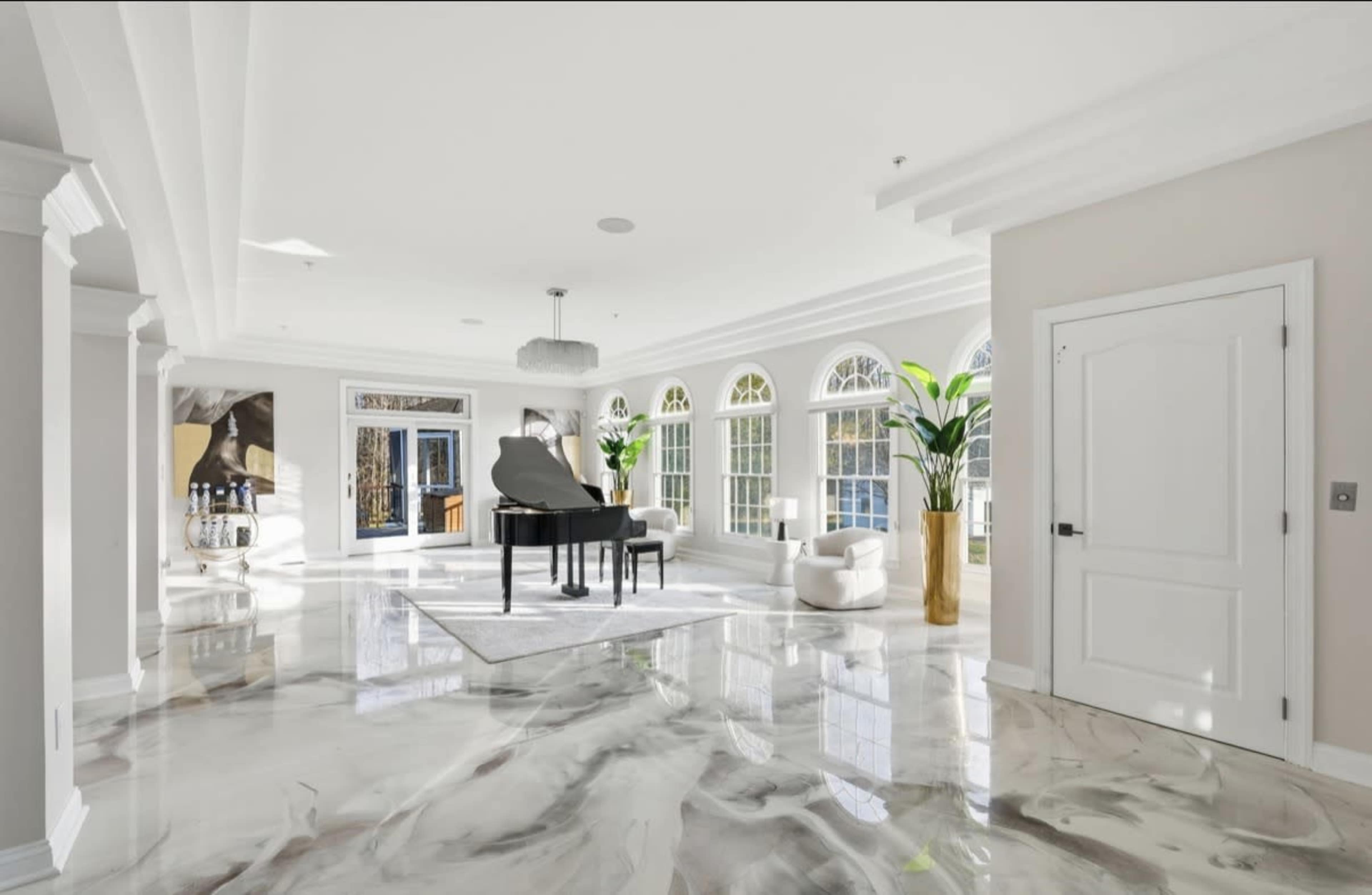 The image shows a spacious, bright interior room featuring a grand piano, large windows, and modern decor.