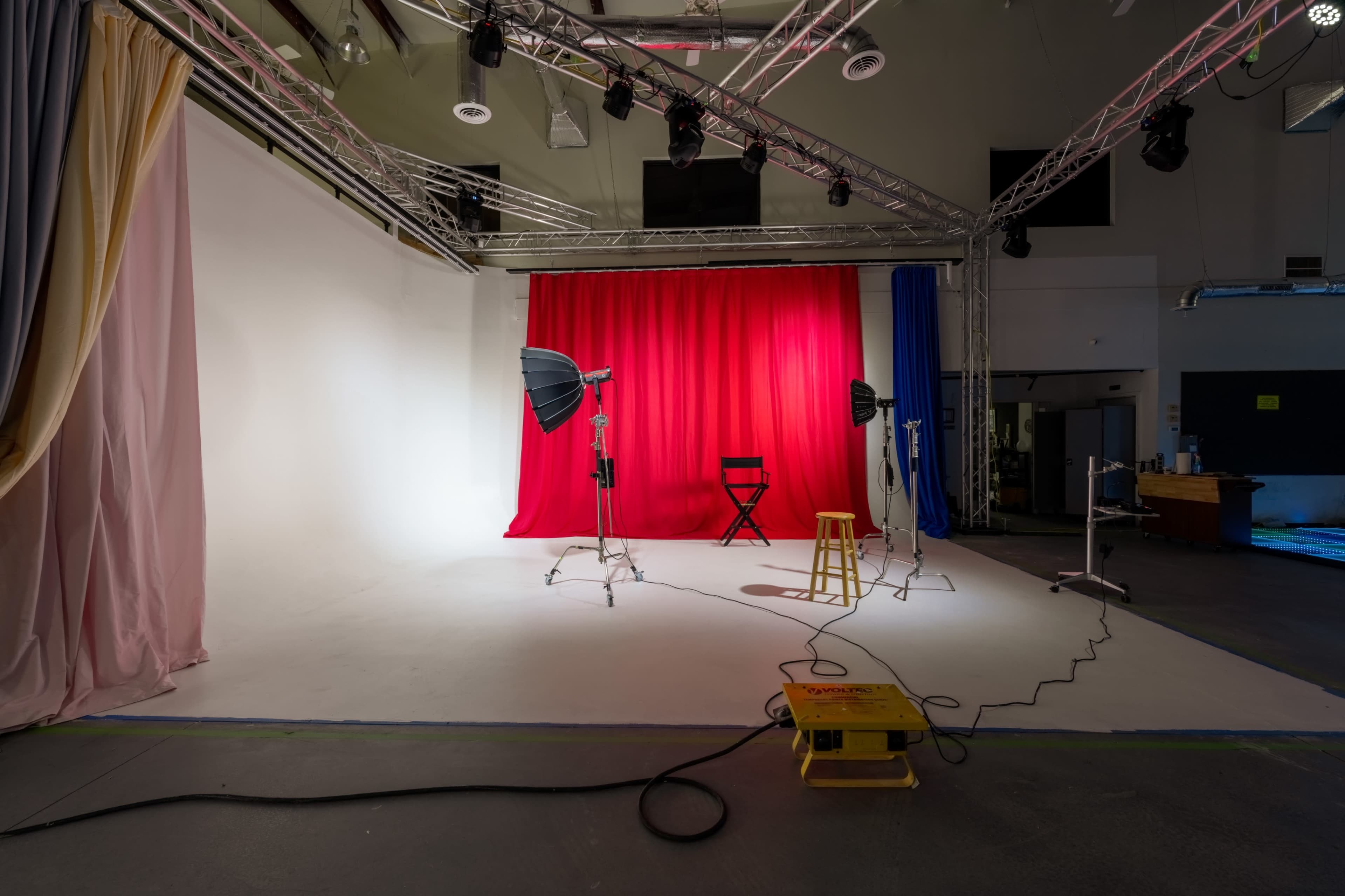 The image shows a photography studio equipped with lighting setups, a red backdrop, and a single chair.