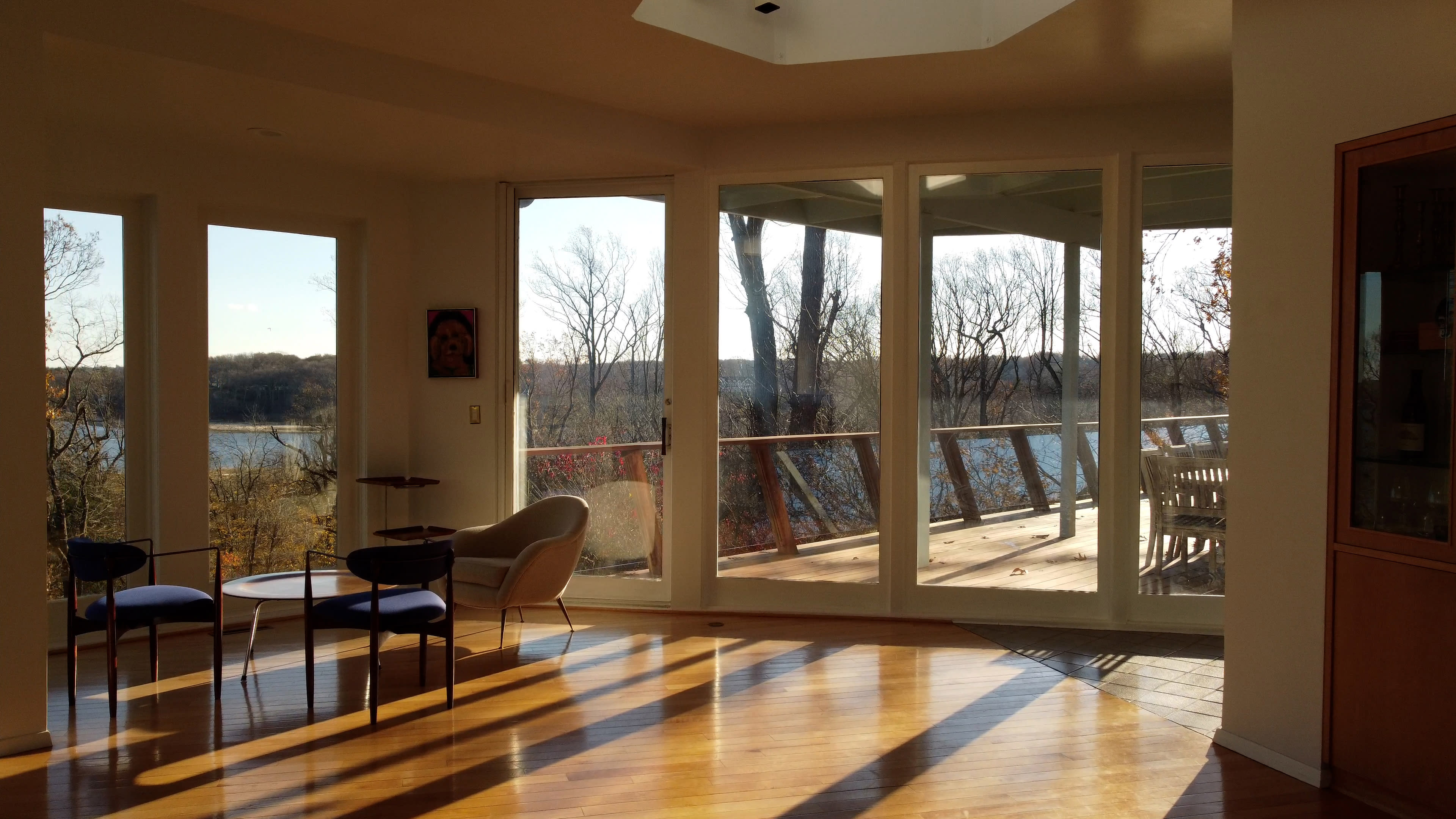 A bright room with large windows overlooks a lake and wooded landscape, featuring a coffee table and a chair.