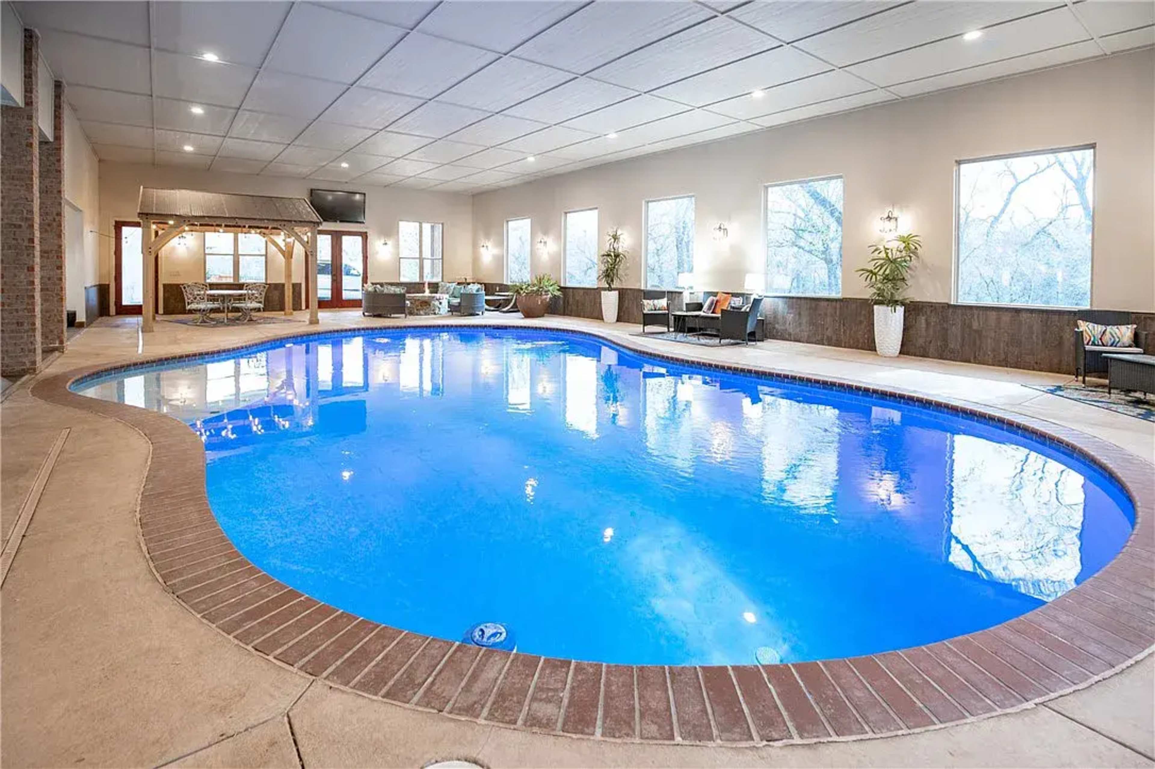 An indoor swimming pool surrounded by a seating area and large windows allowing natural light.