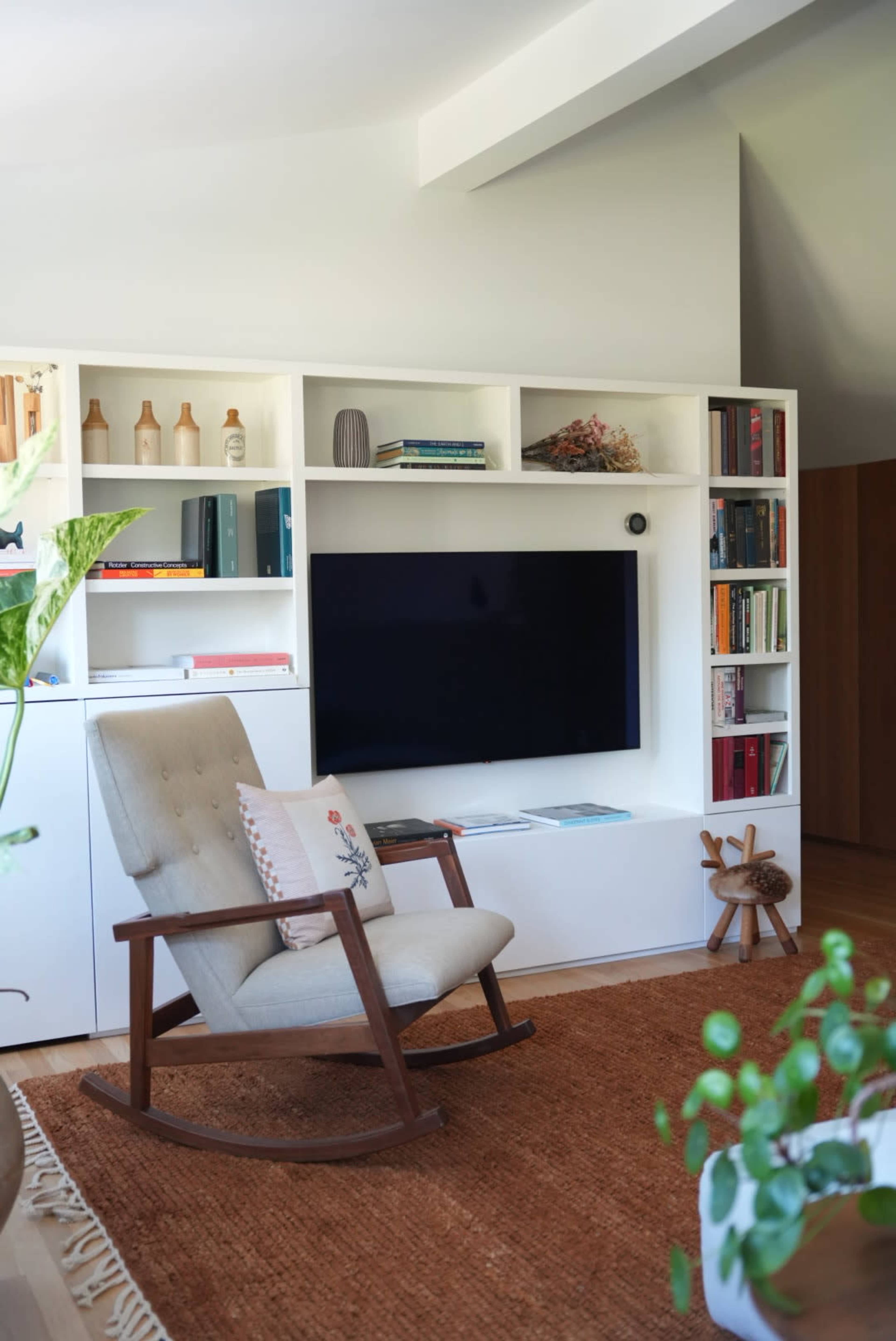 A modern living room features a rocking chair in front of a white media console with shelves displaying books and decorative items.