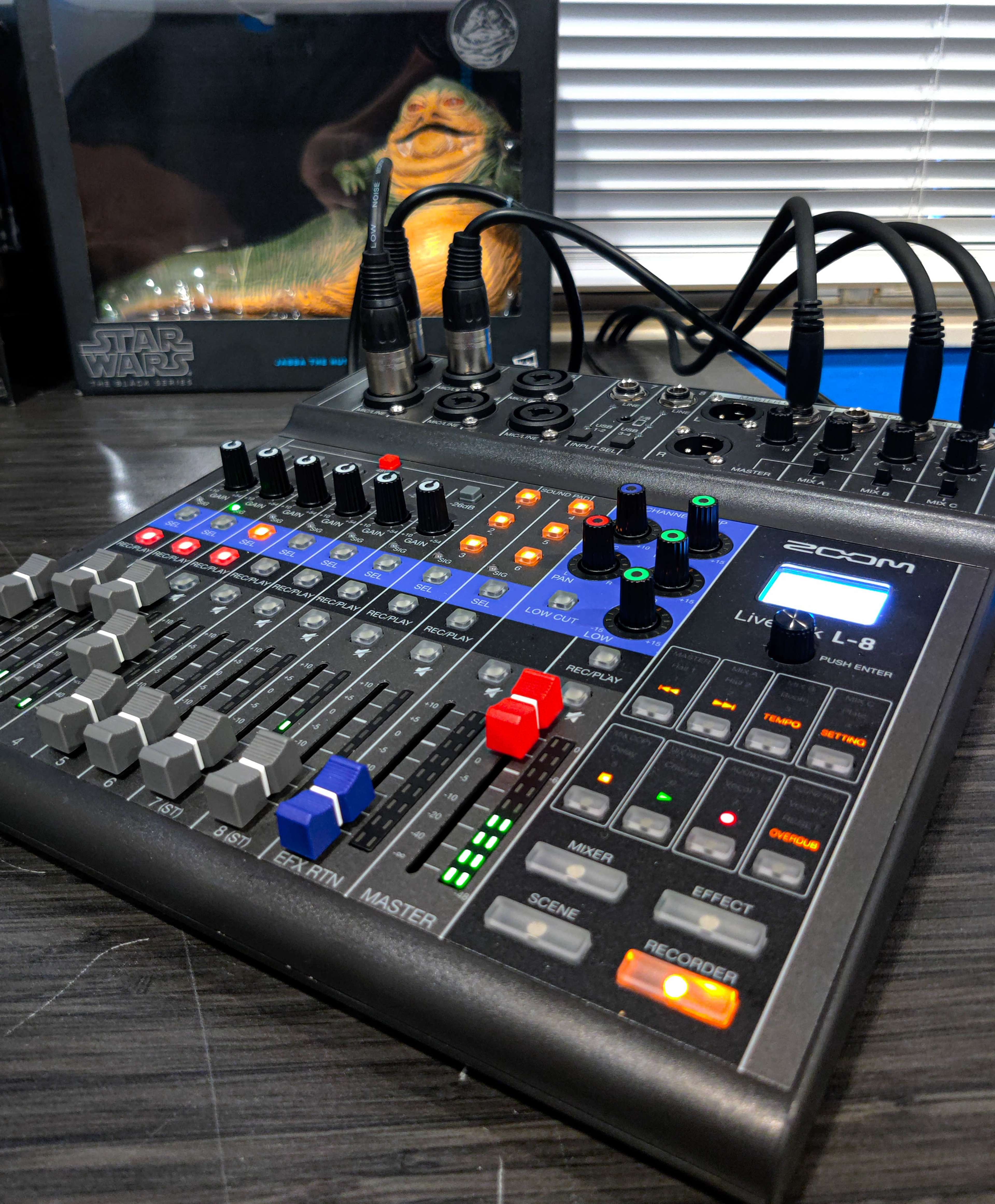 A Zoom L-8 mixer with various control knobs and buttons, placed on a table next to a Star Wars-themed item.