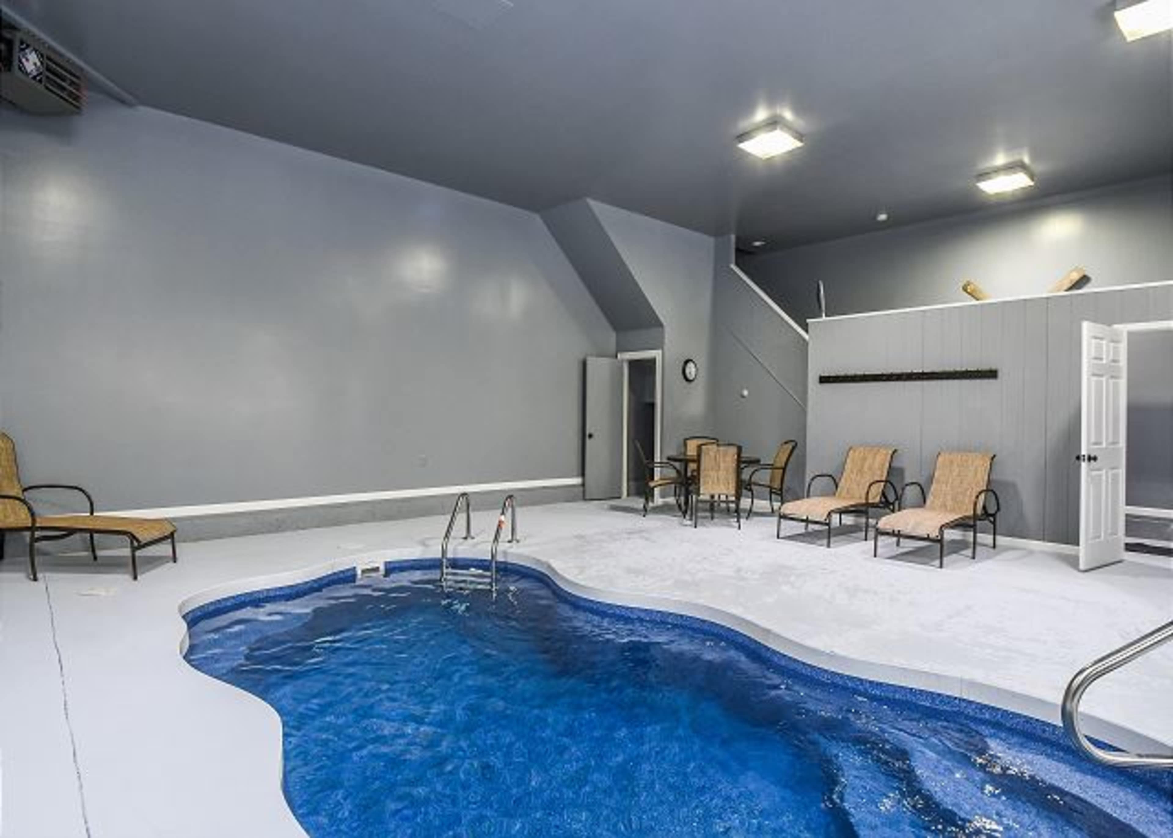 The image shows an indoor pool area with a small pool and several lounge chairs arranged around it.