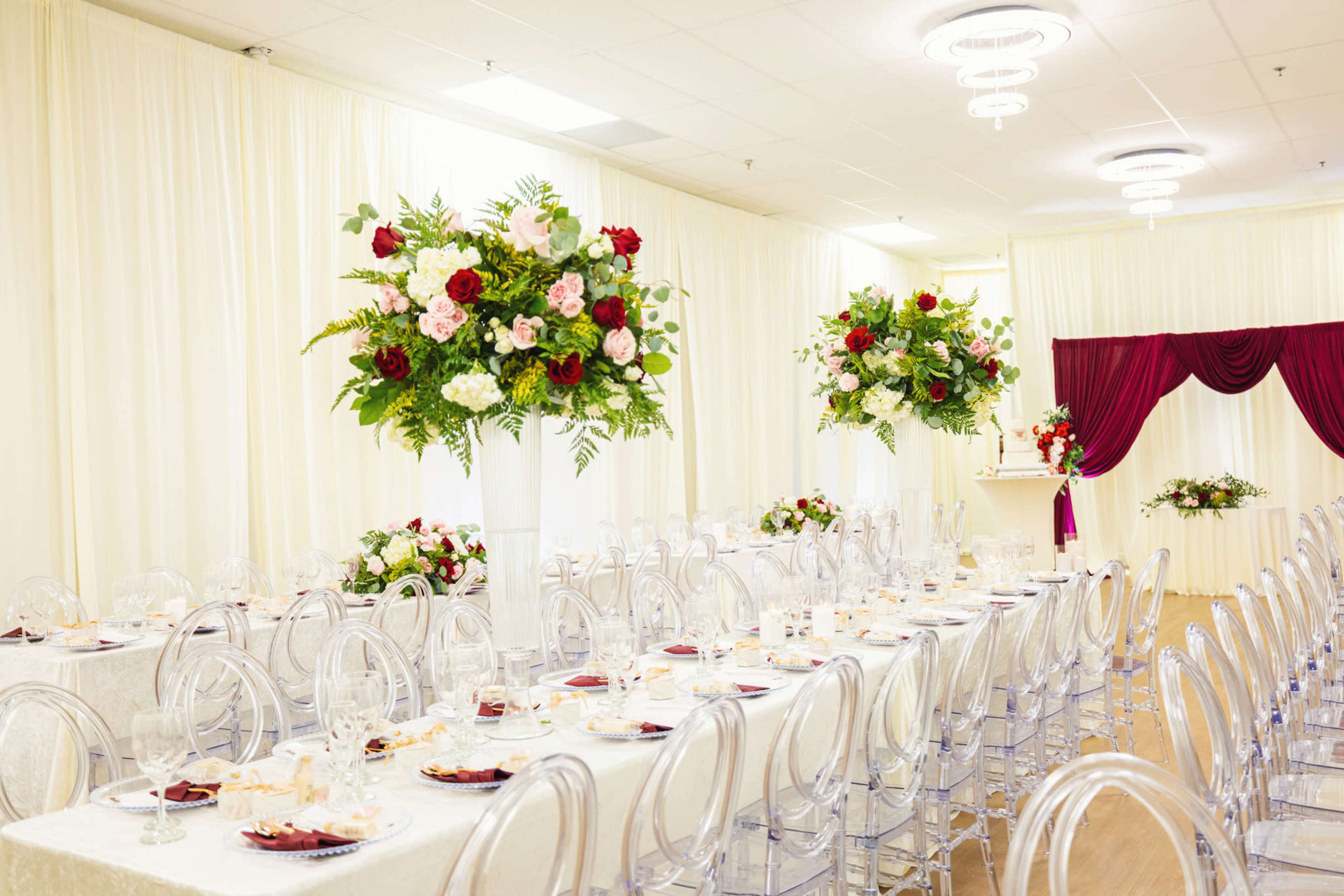 A banquet hall is set up with long tables adorned with elegant tableware and tall floral centerpieces.