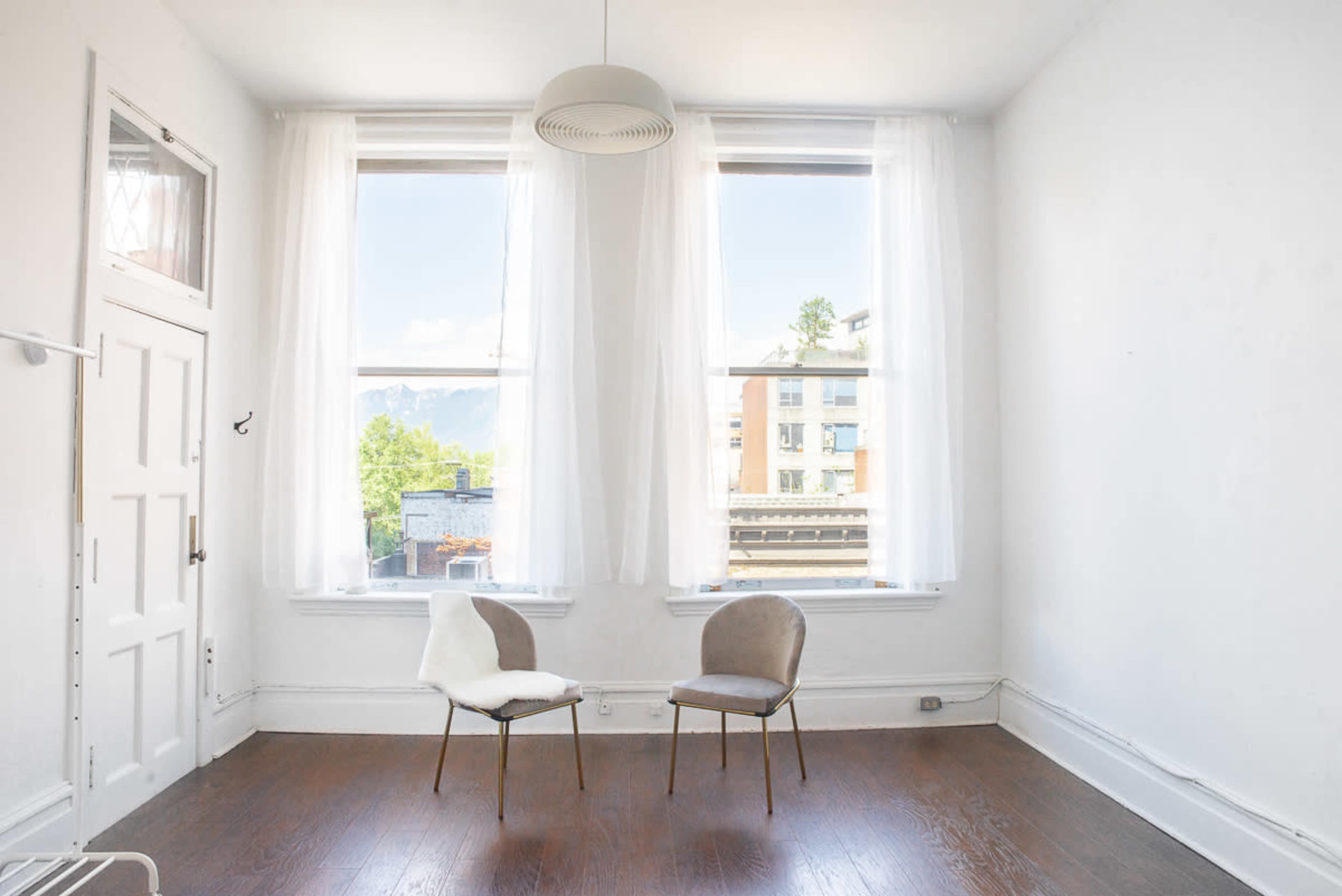 A bright, minimalistic room with two chairs near large windows and white walls.