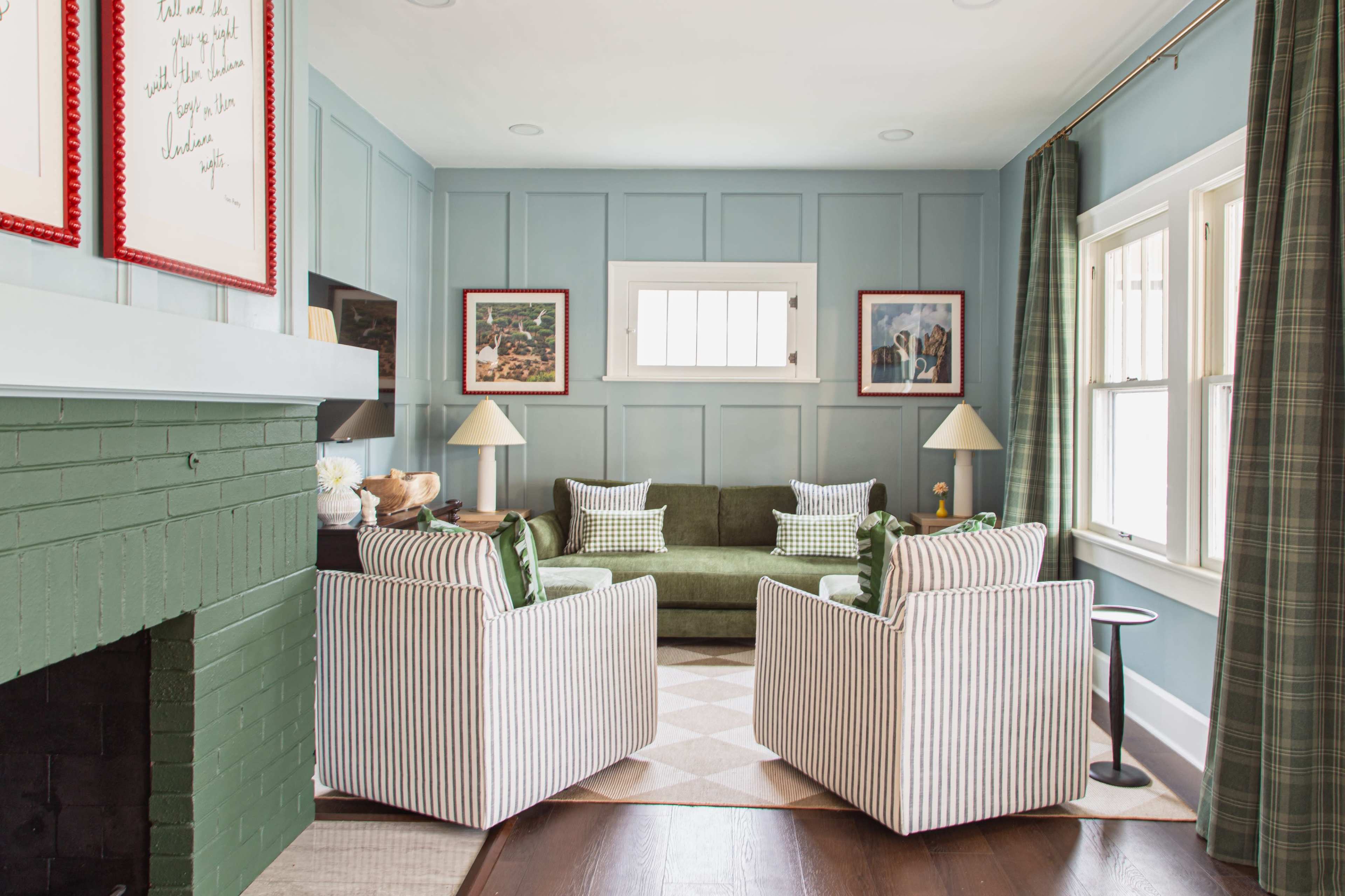 The image shows a cozy living room featuring a green sofa against a blue paneled wall, flanked by two striped armchairs and a small side table.