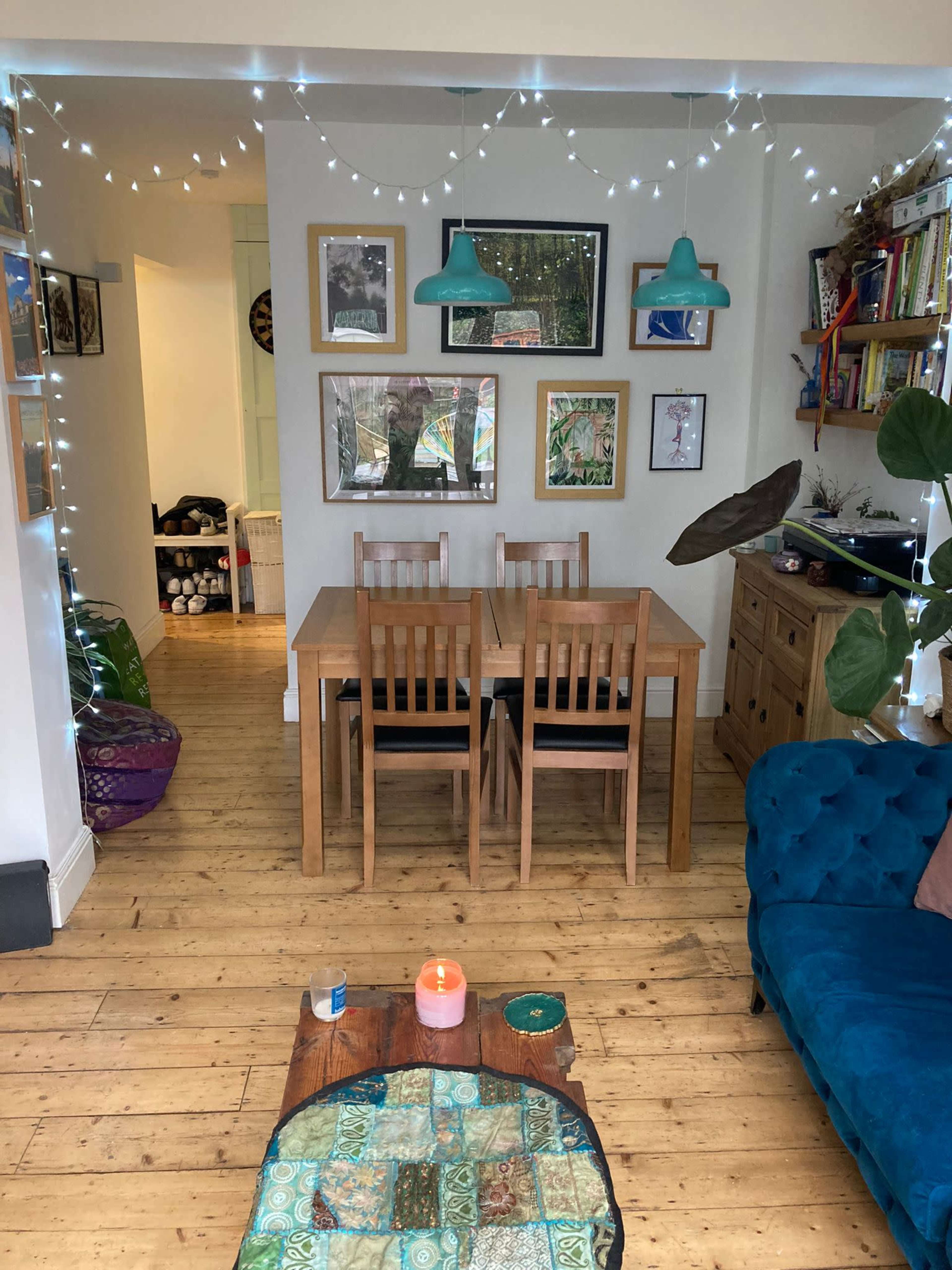 A dining area with a wooden table and chairs is illuminated by pendant lights and adorned with framed pictures on the walls.