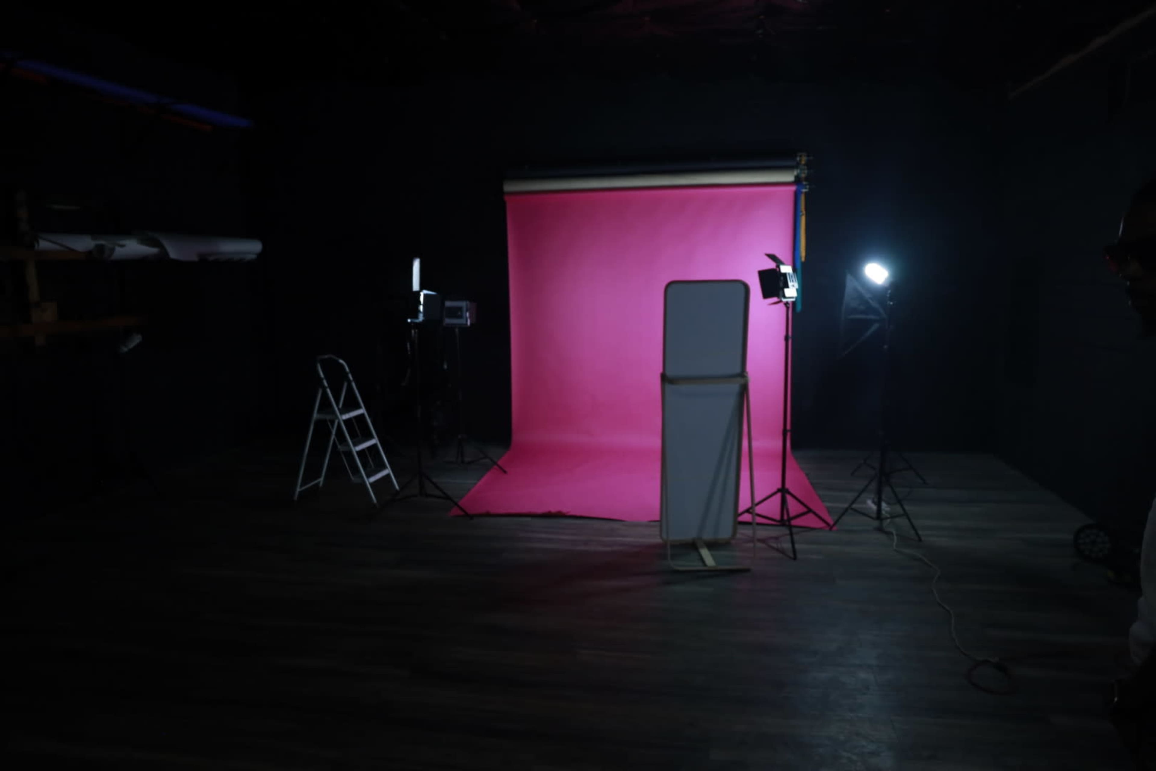 A photography studio with a pink backdrop, lighting equipment, and a ladder positioned nearby.