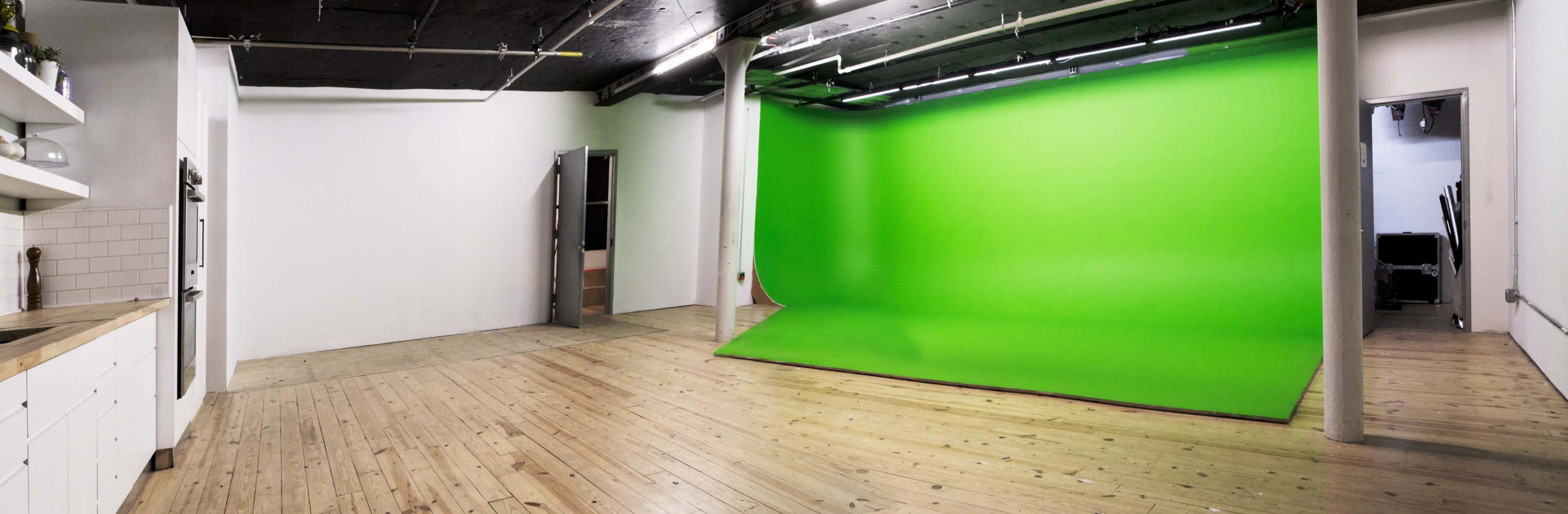 The image shows a spacious studio with wooden flooring, featuring a large green screen backdrop and an open door leading to another area.