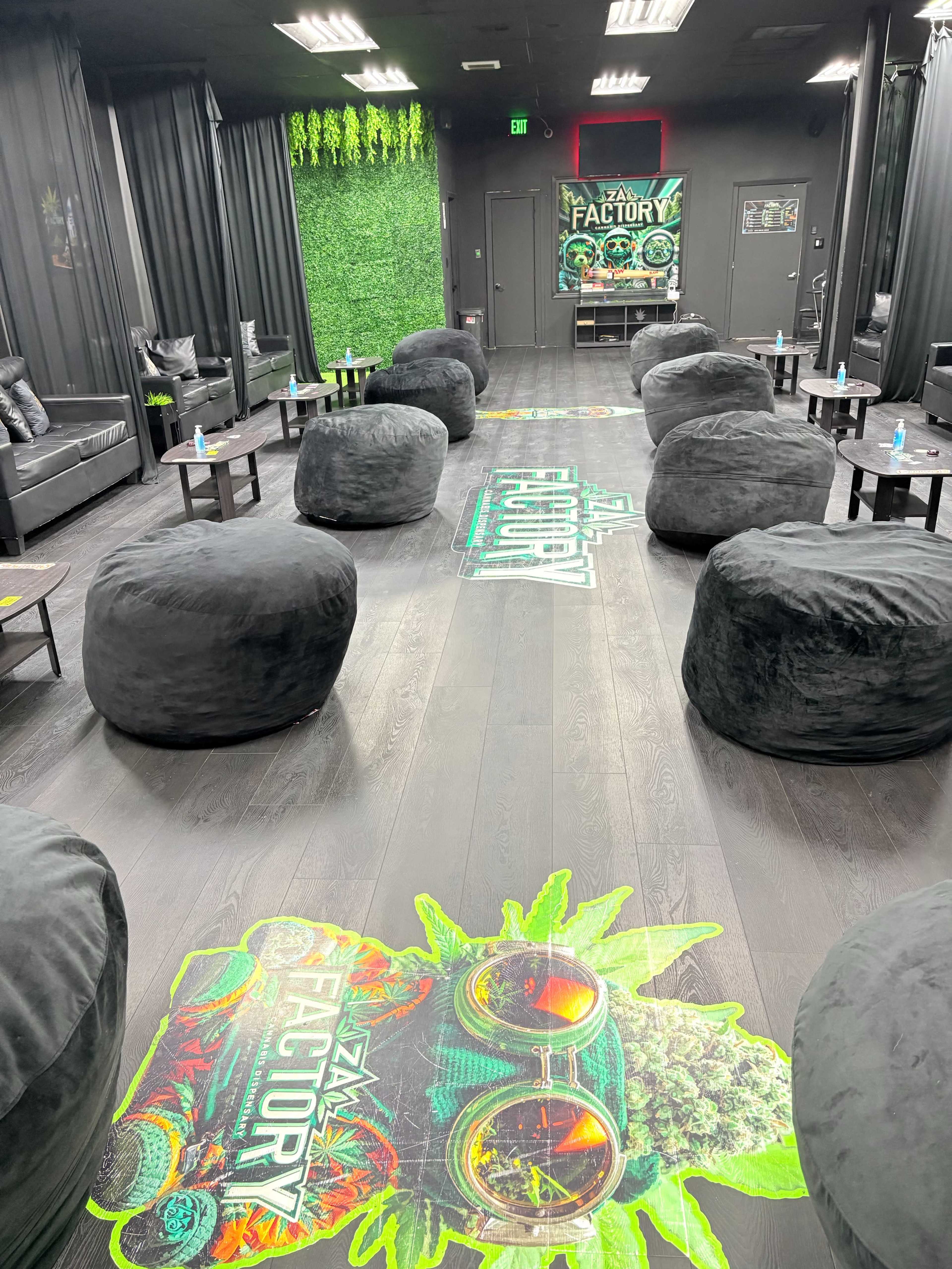 The image shows a modern lounge area with large, round black bean bags, small tables, and vibrant green accents on the walls and floor, creating a casual, inviting atmosphere.