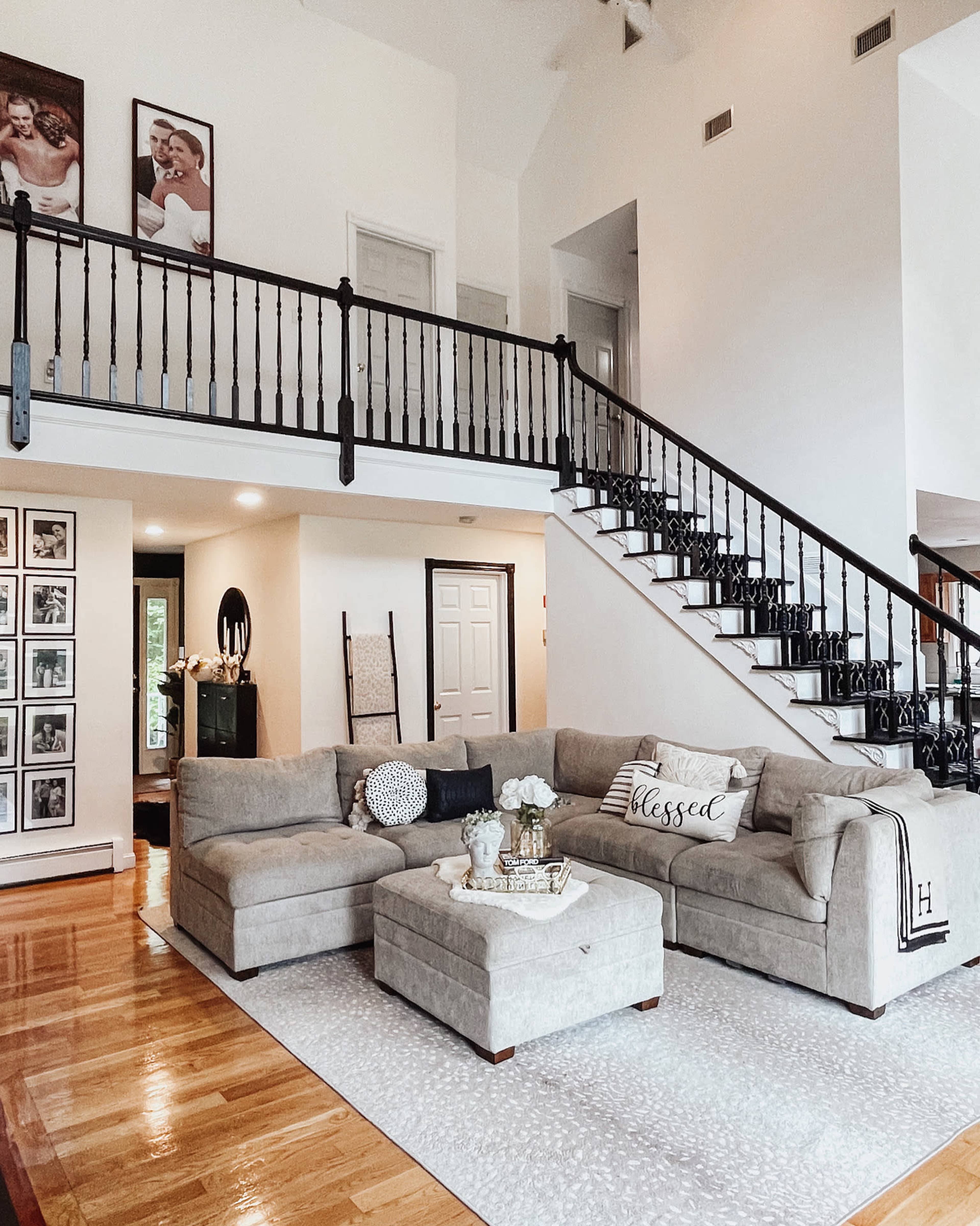 A spacious living room with a large sectional sofa, a coffee table, and a staircase leading to an upper level, all set against a bright, neutral color palette.