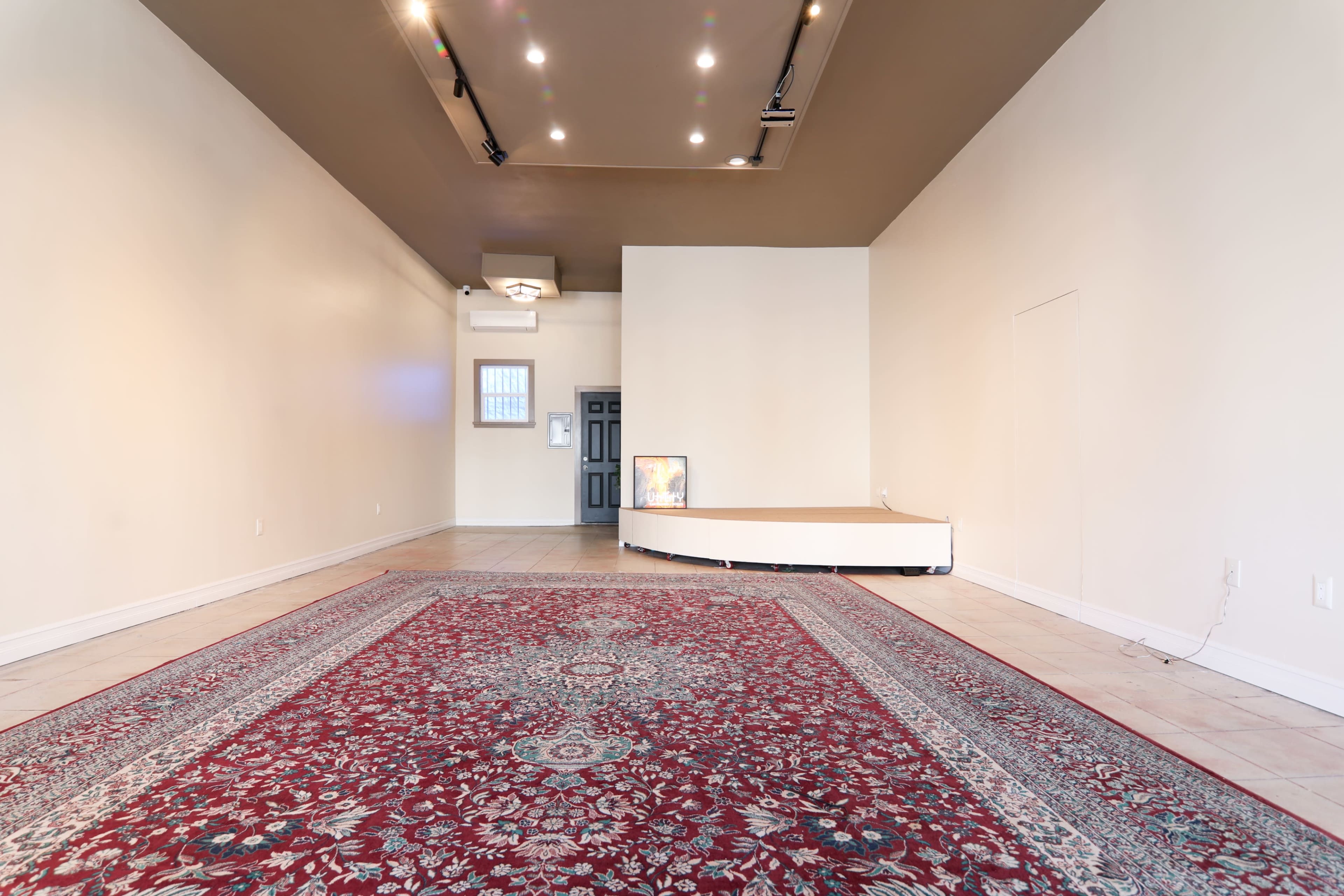 An empty room with a large rug, a small raised platform, and a door at the far end.