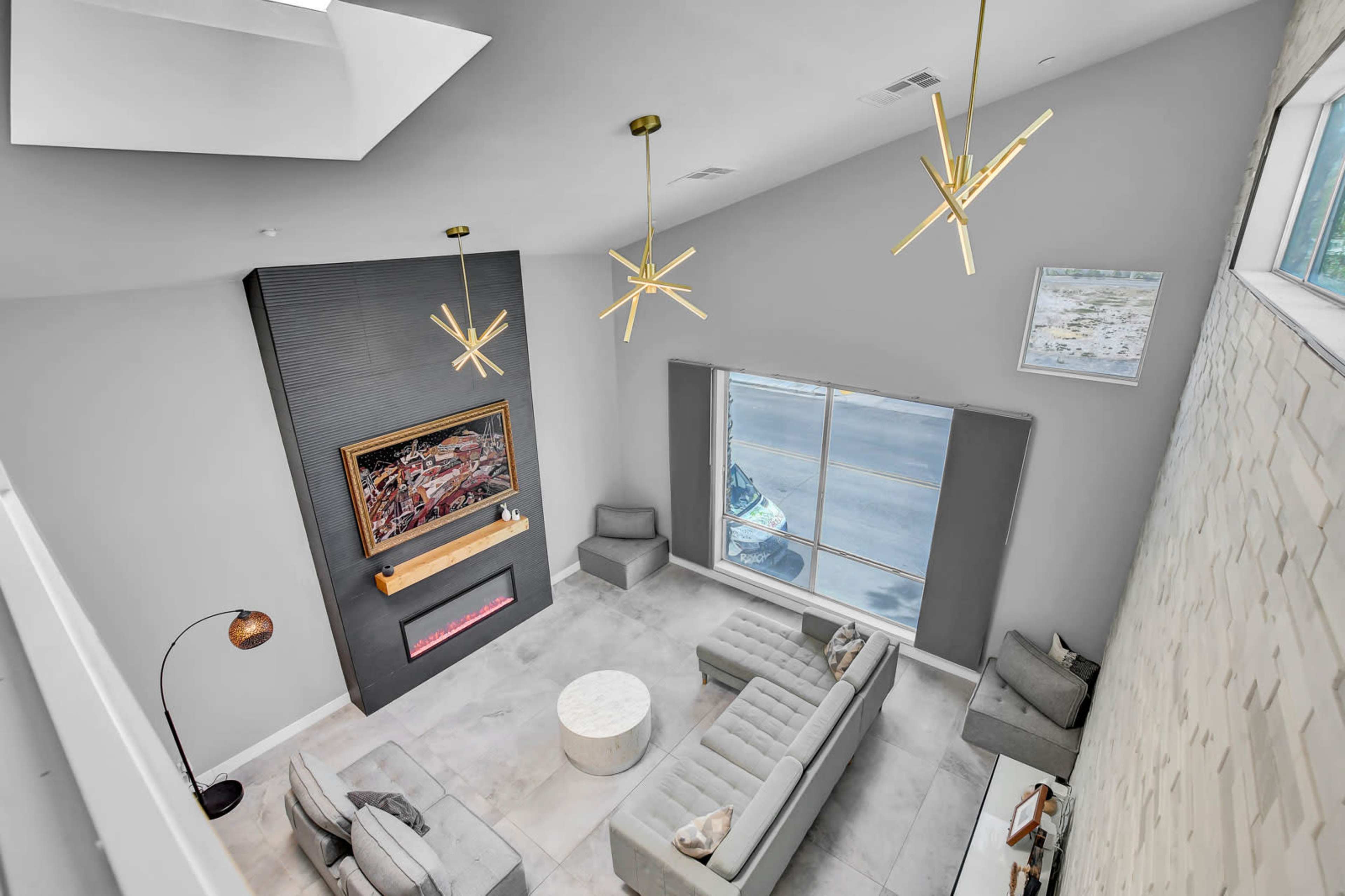 The image shows a modern living room featuring a seating area with a light gray sectional sofa, a circular coffee table, and a decorative wall-mounted electric fireplace.