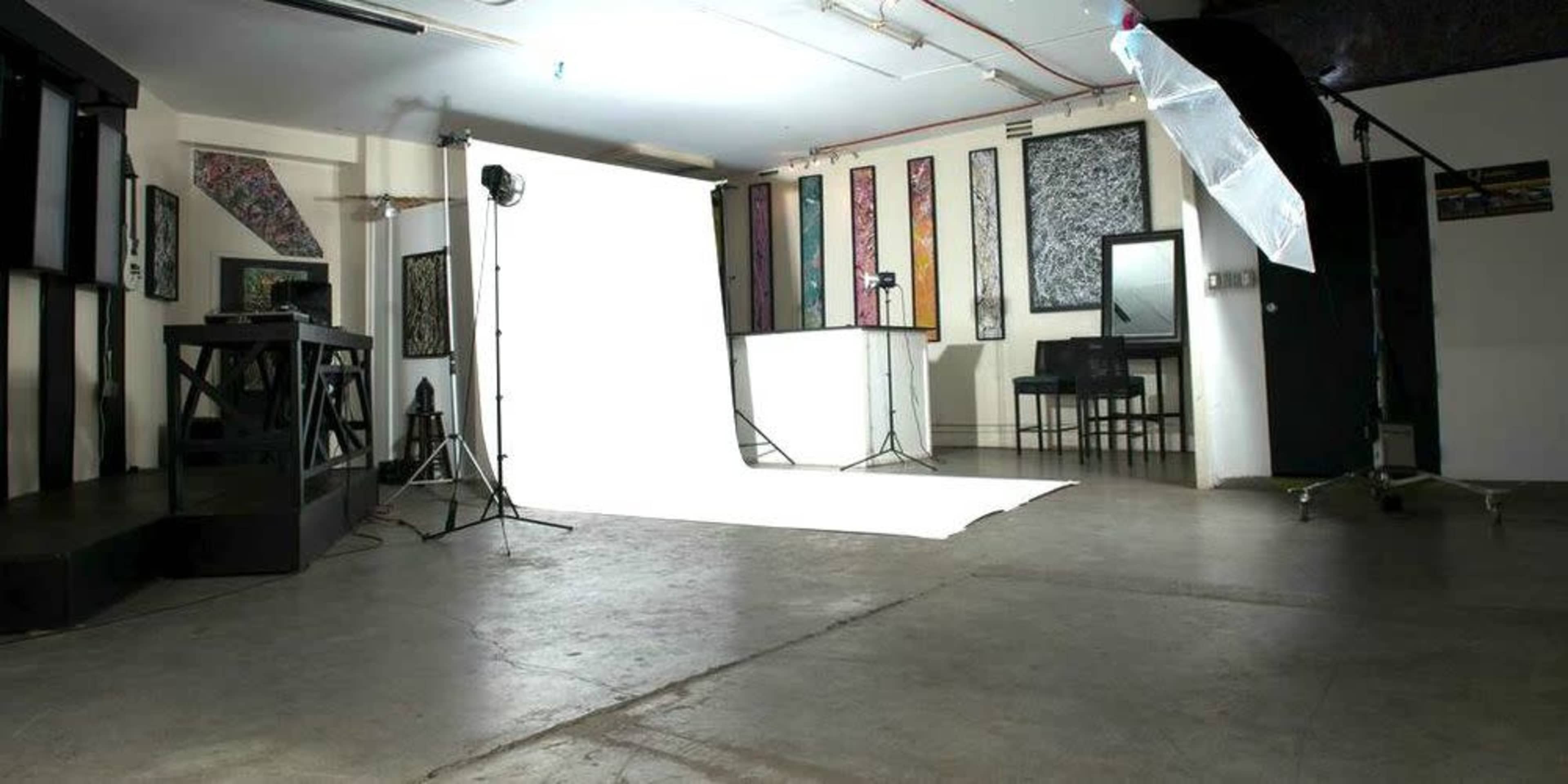 The image shows a photography studio with a white backdrop, lighting equipment, and minimalist furnishings.