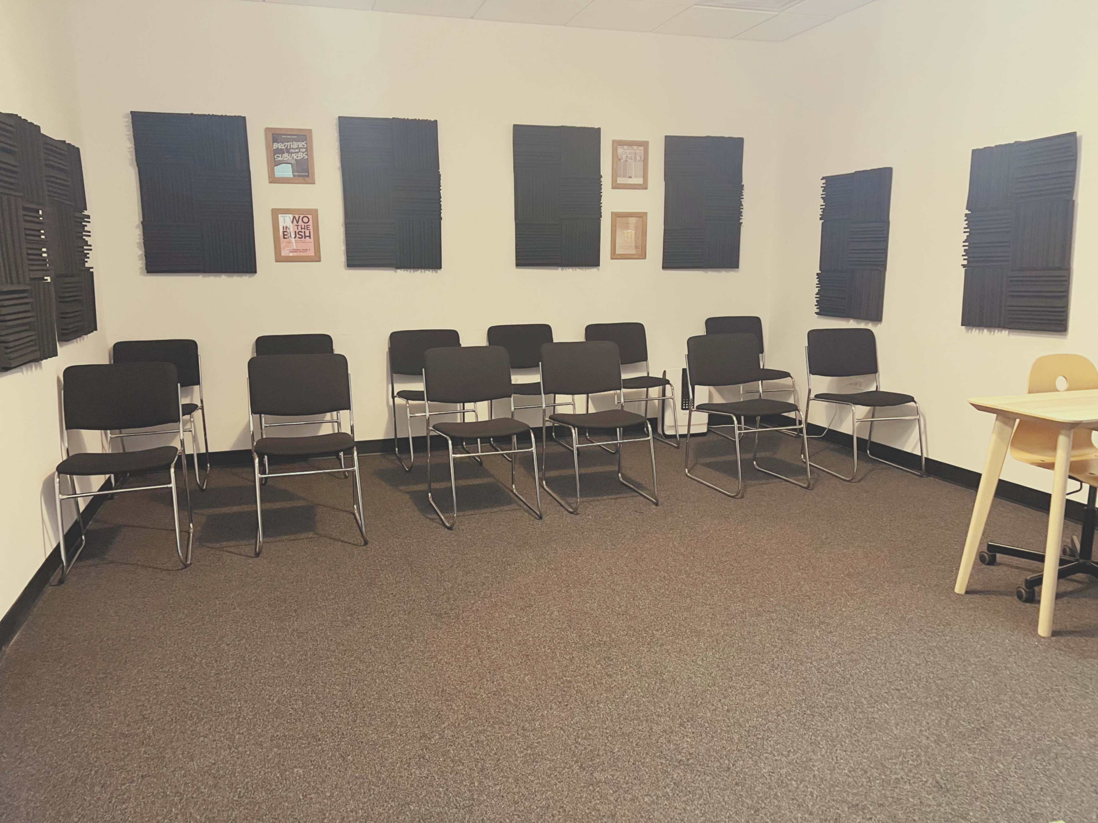 The image shows a vacant room with a row of black chairs facing a wall, and soundproofing panels mounted on the walls.