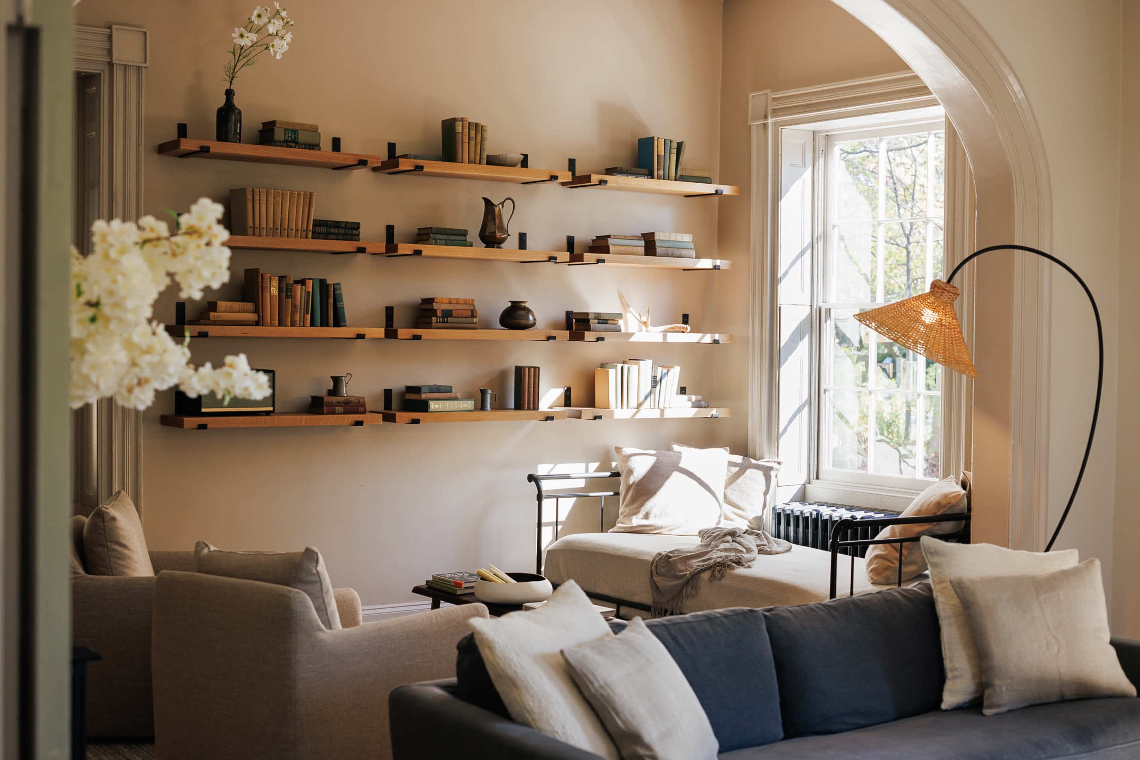 A cozy living room features a wall of wooden shelves filled with books and decorative items, complemented by comfortable seating and a nearby window letting in natural light.