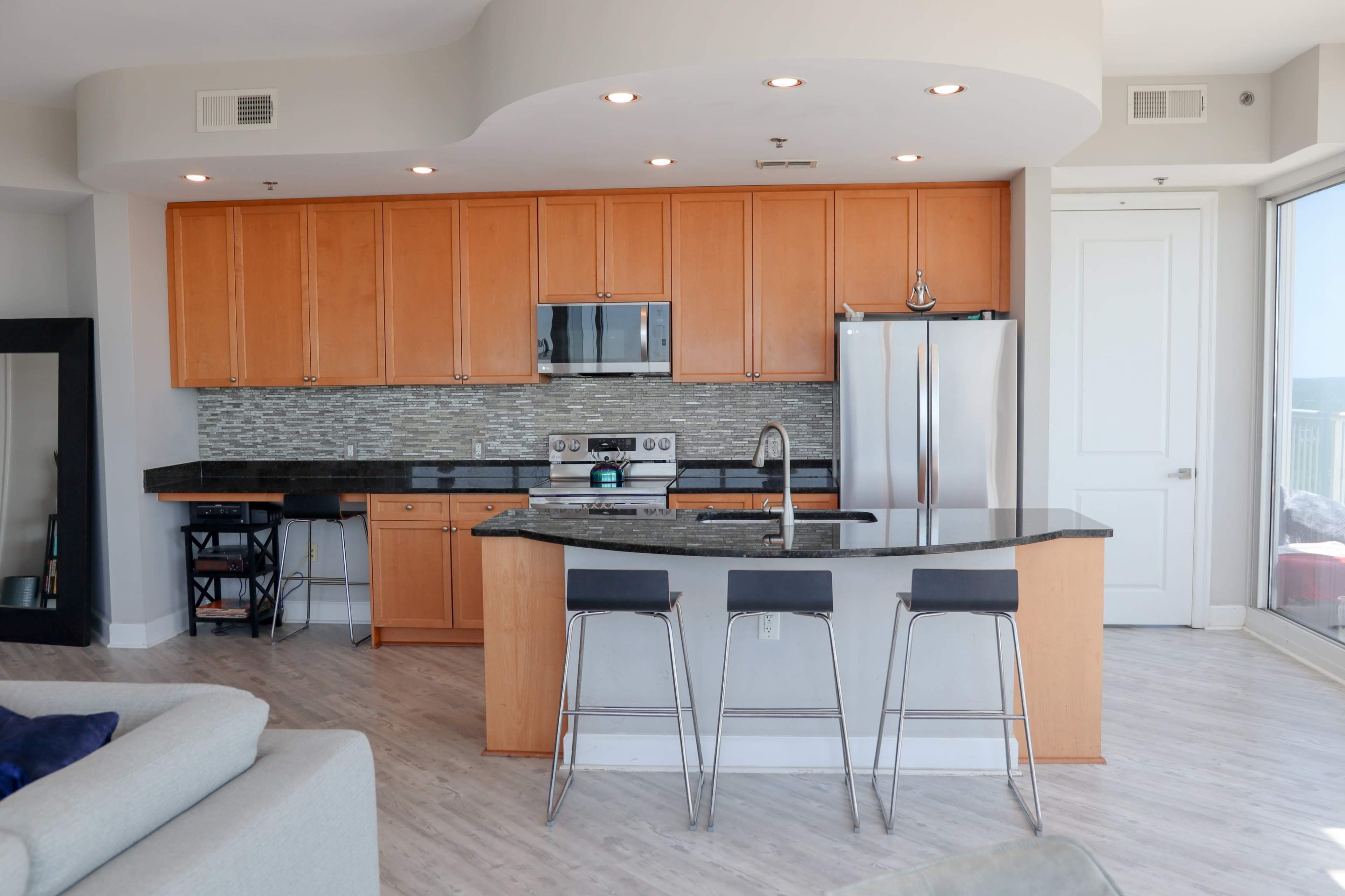 A modern kitchen featuring wooden cabinets, stainless steel appliances, and a granite-topped island with bar stools.
