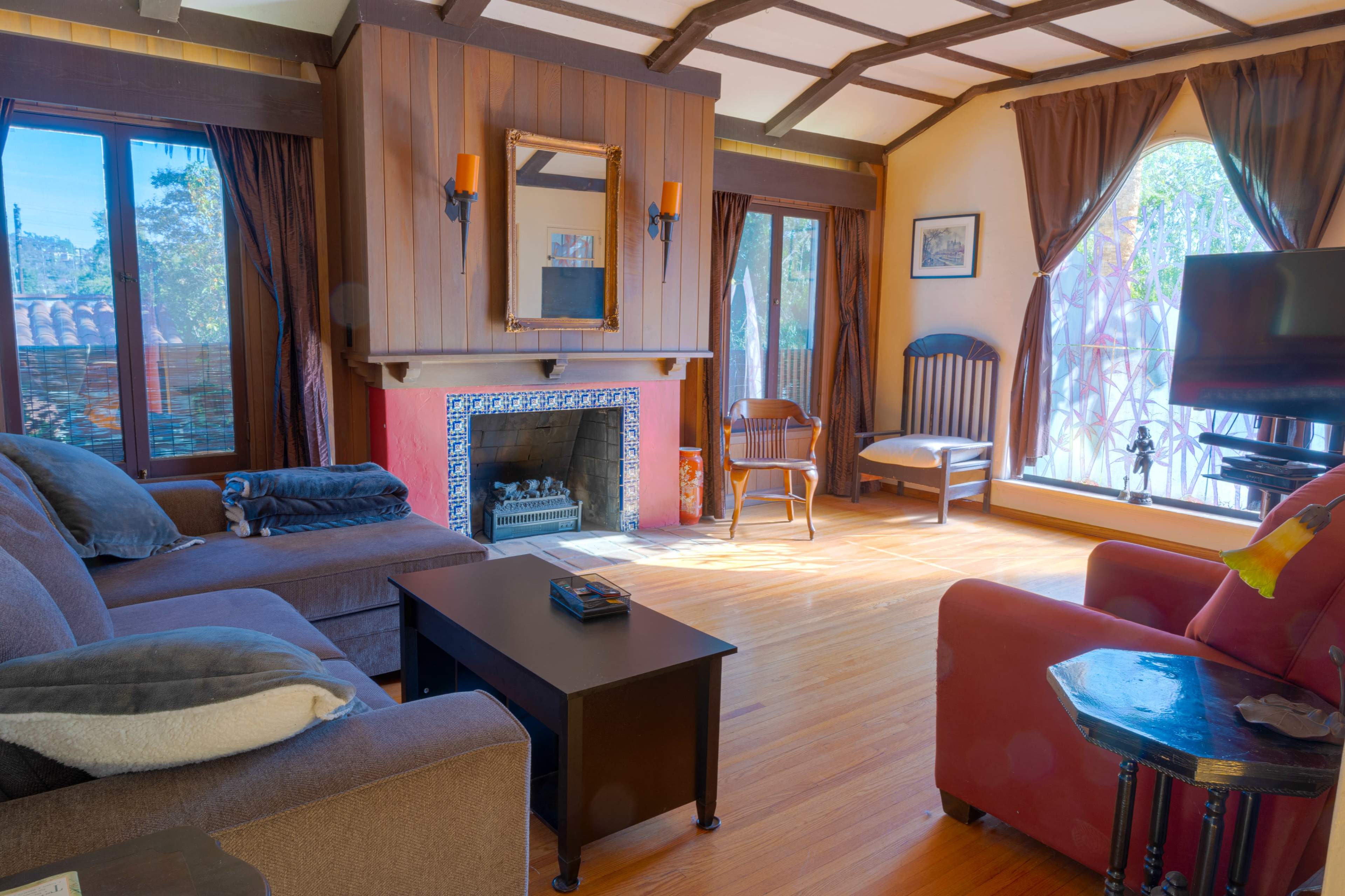 A cozy living room featuring a fireplace, a large sofa, a coffee table, and large windows with curtains.
