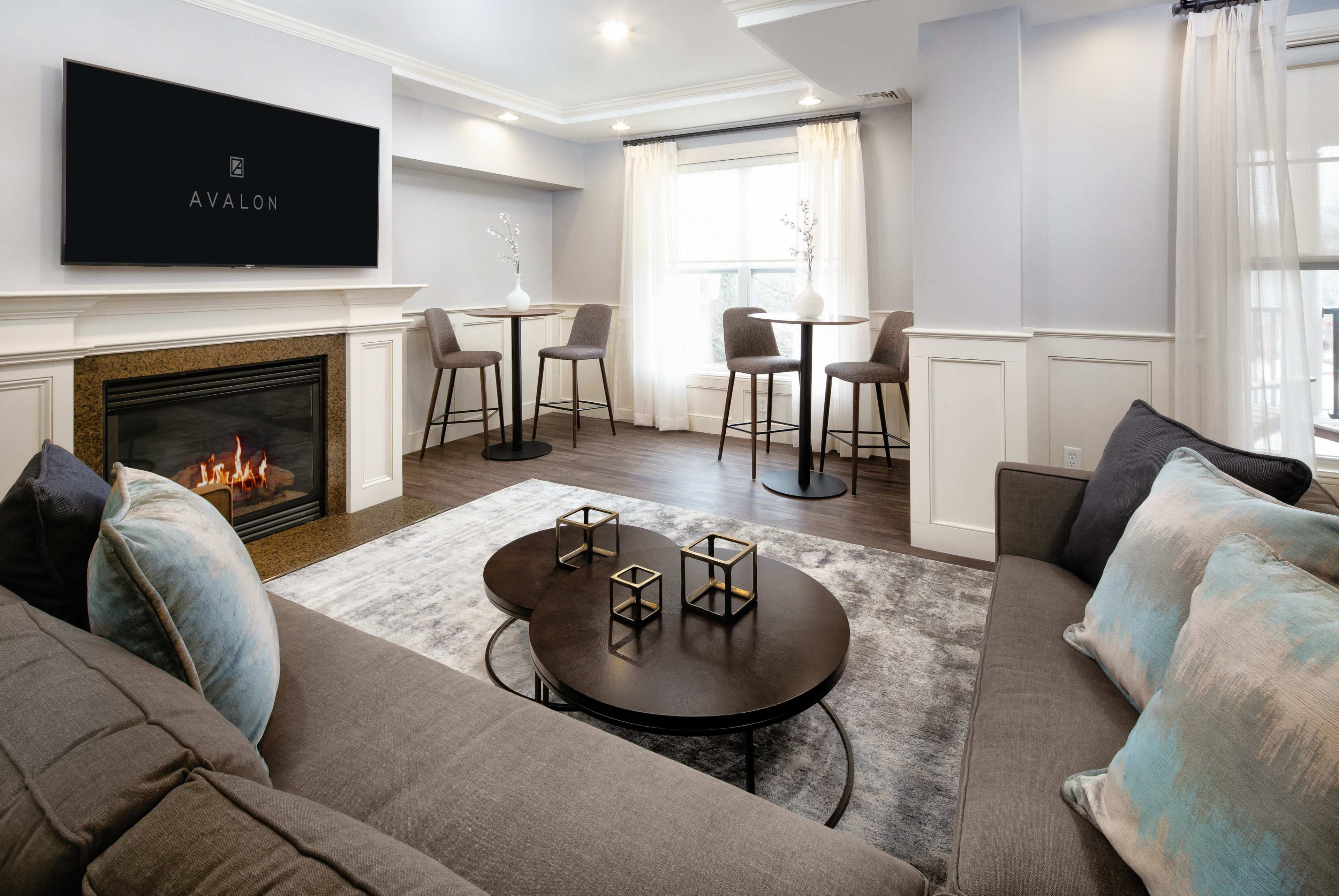 A modern living room with a fireplace, a cozy sofa, and a small dining area featuring high stools and a round table.